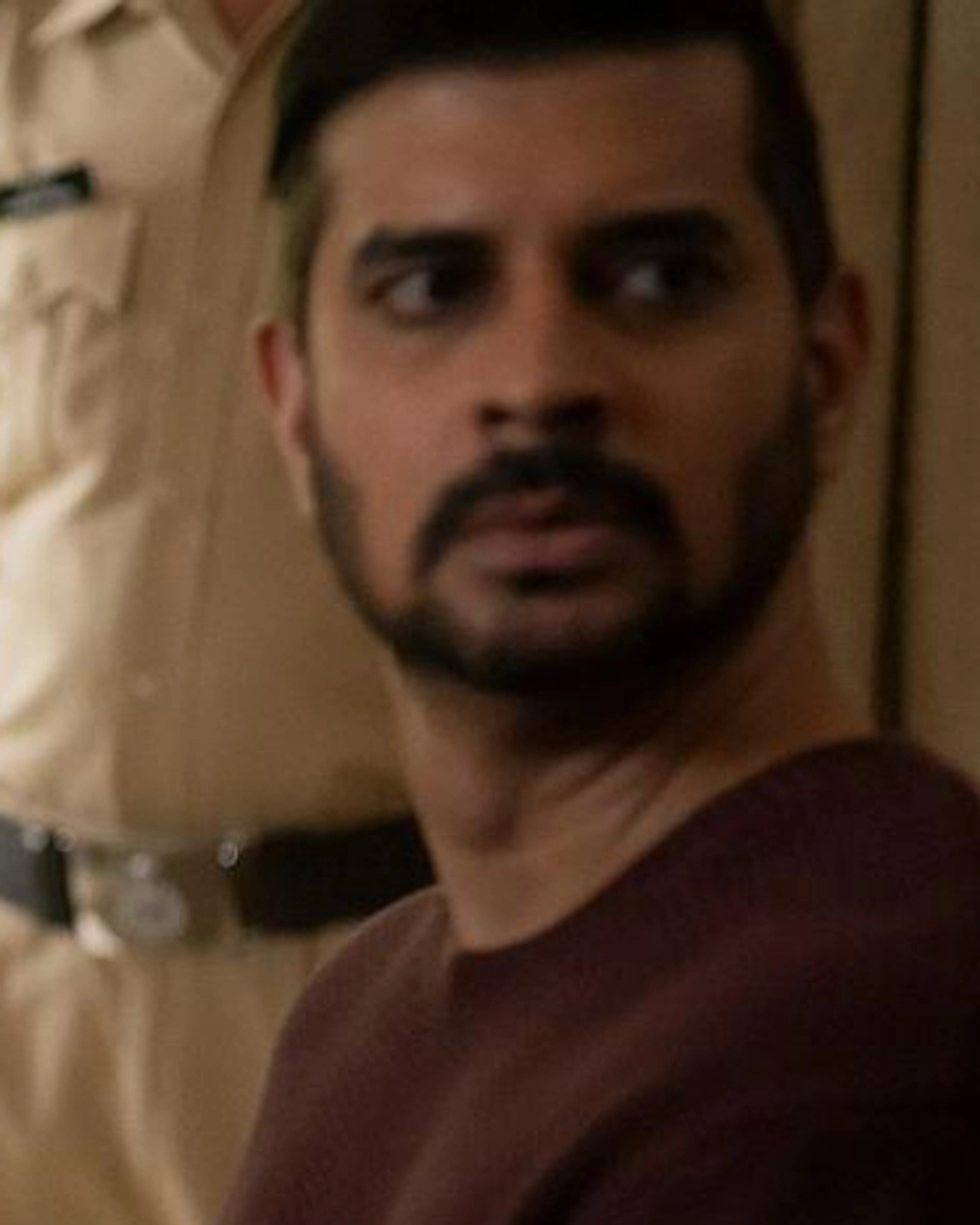 Parineeti Chopra as Anvita and Tahir Raj Bhasin as Alok look towards someone in a police station, with a uniformed officer behind them.