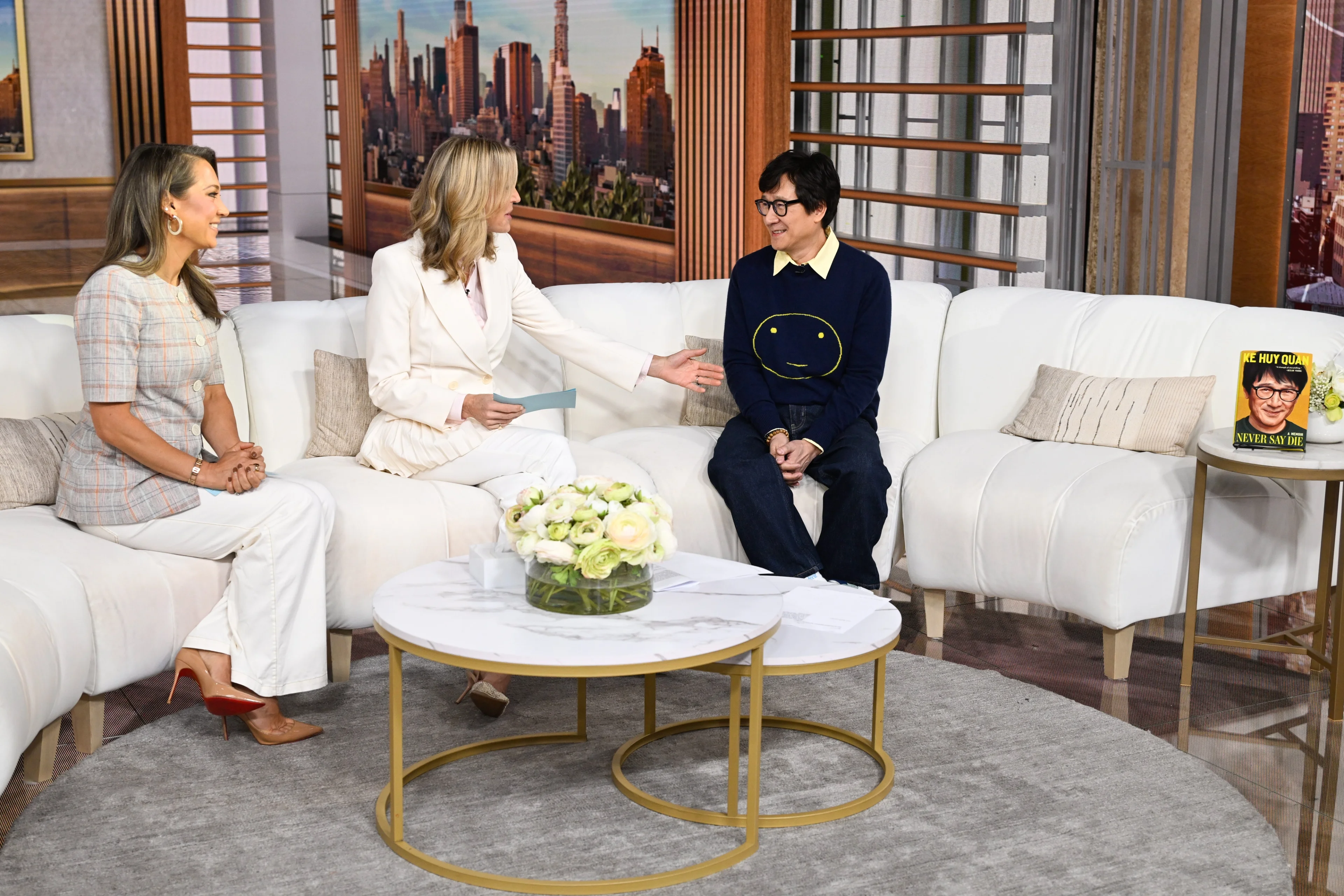 Ke Huy Quan speaks with Ginger Zee and Lara Spencer, with Never Say Die displayed beside them.