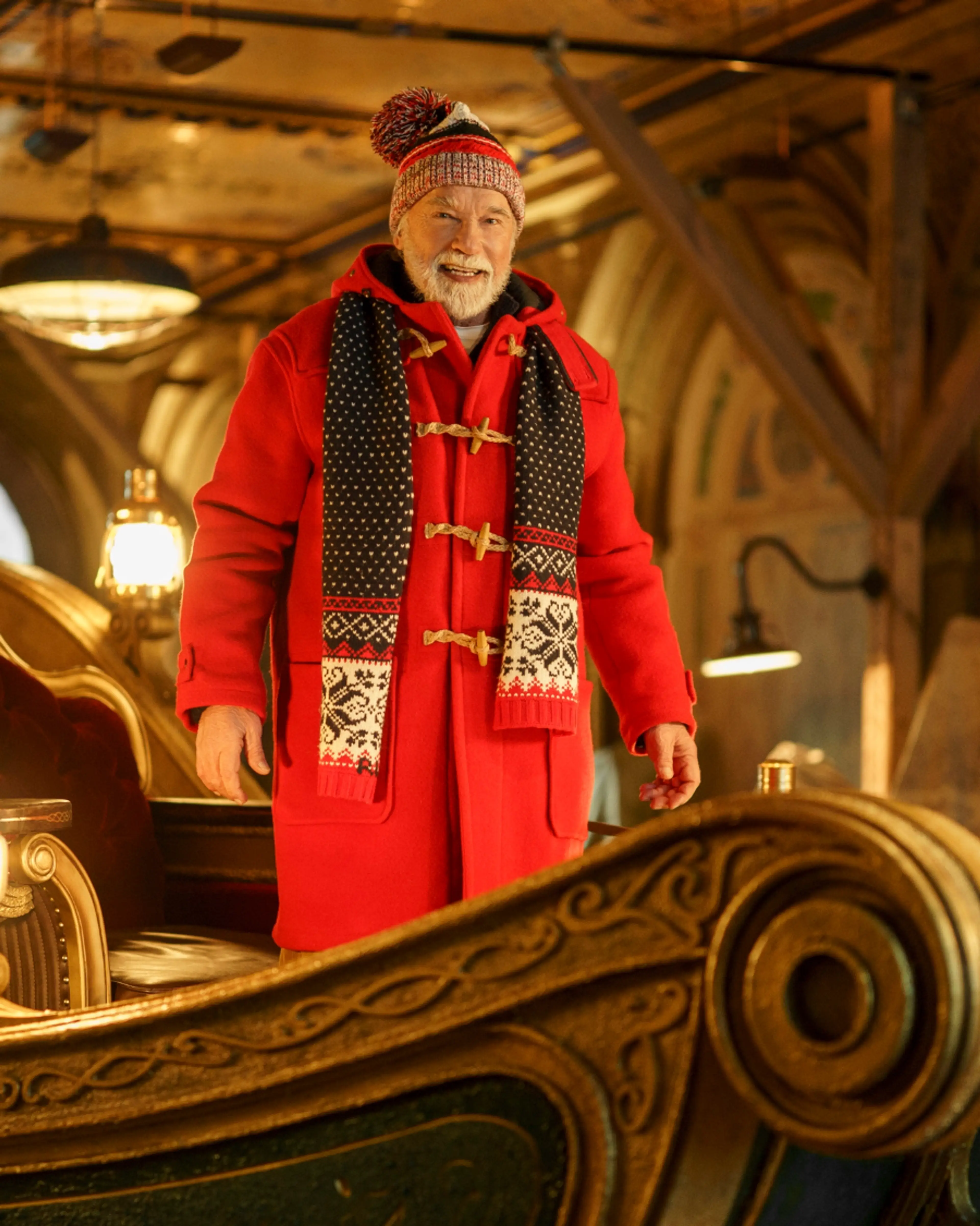 Arnold Schwarzenegger as Santa, wearing a red coat and knit hat on an ornate sleigh.