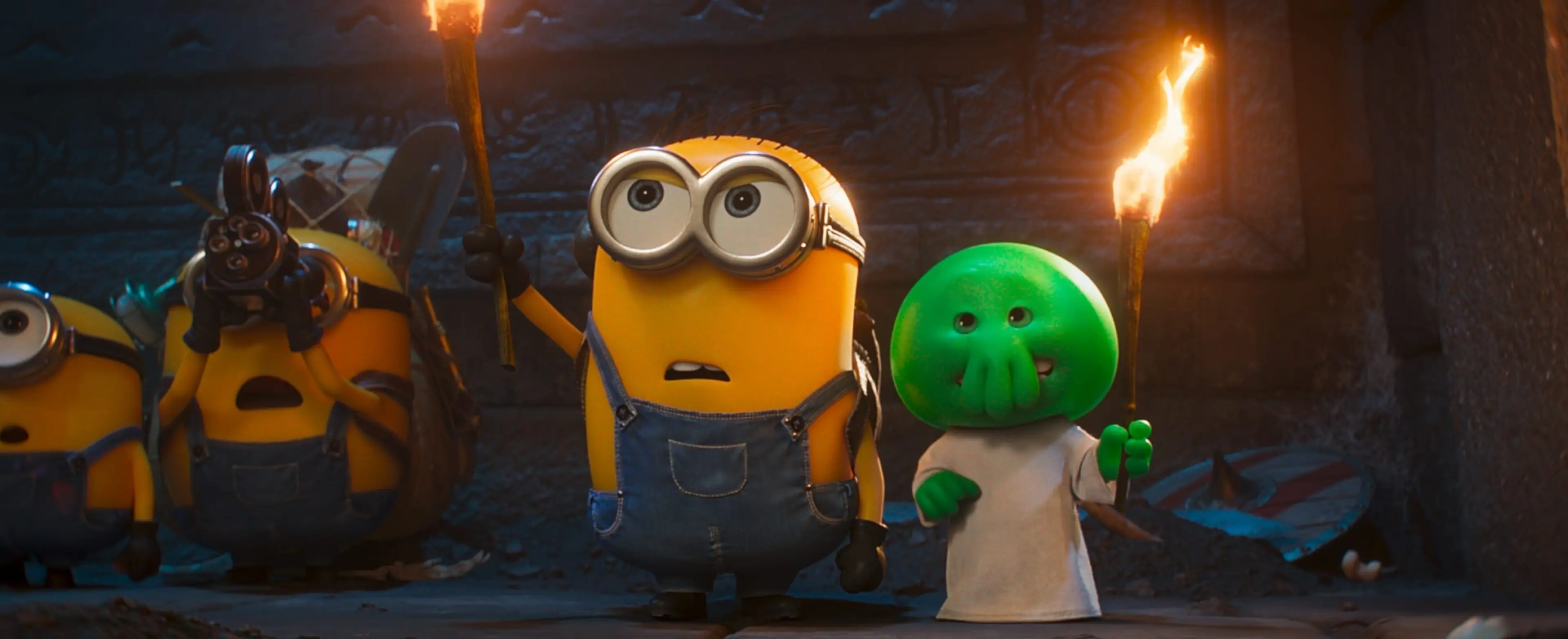 Minions stand with a small green monster near torchlight in Minions & Monsters.