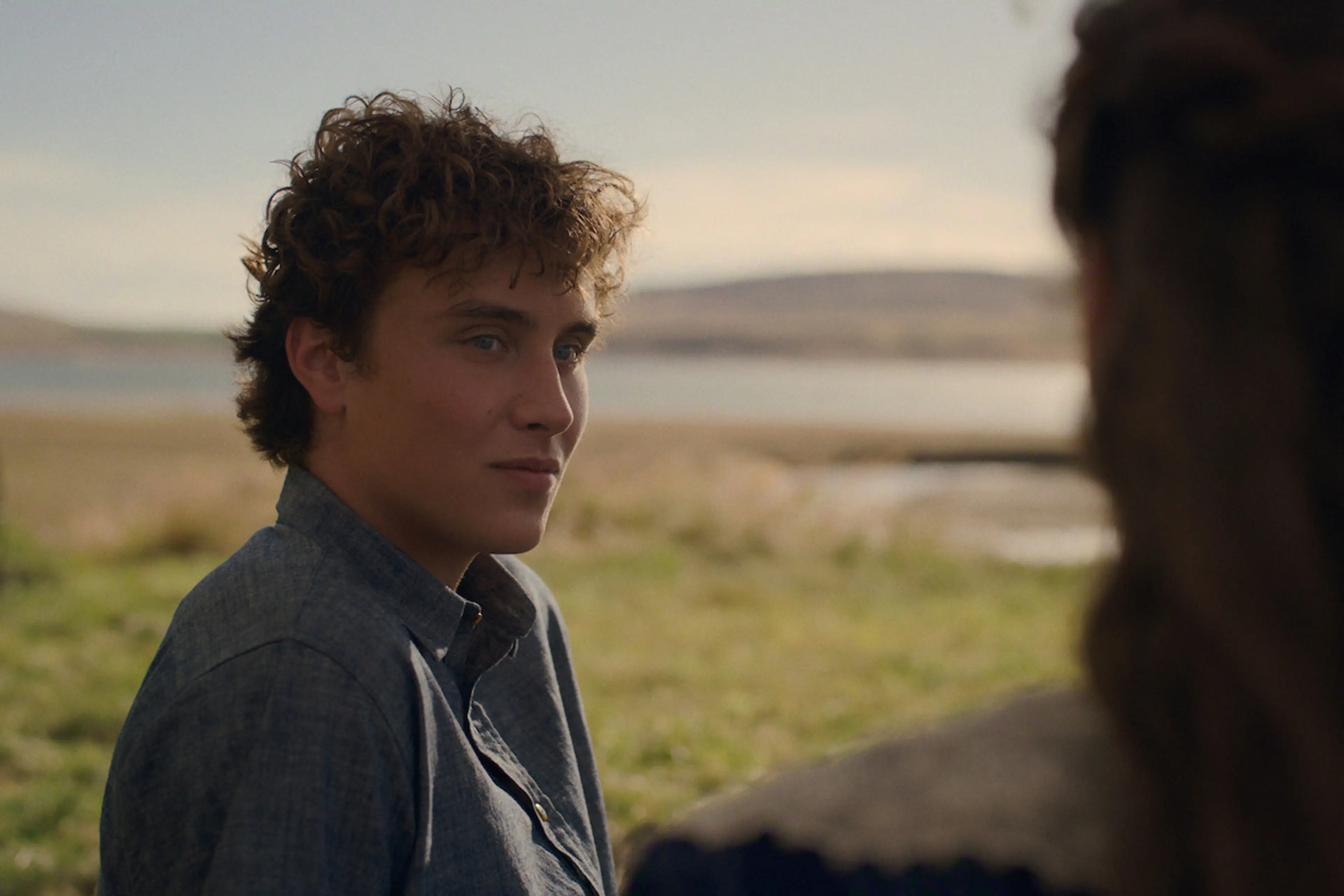 A young man in period clothing looks across a coastal field in East of Eden.