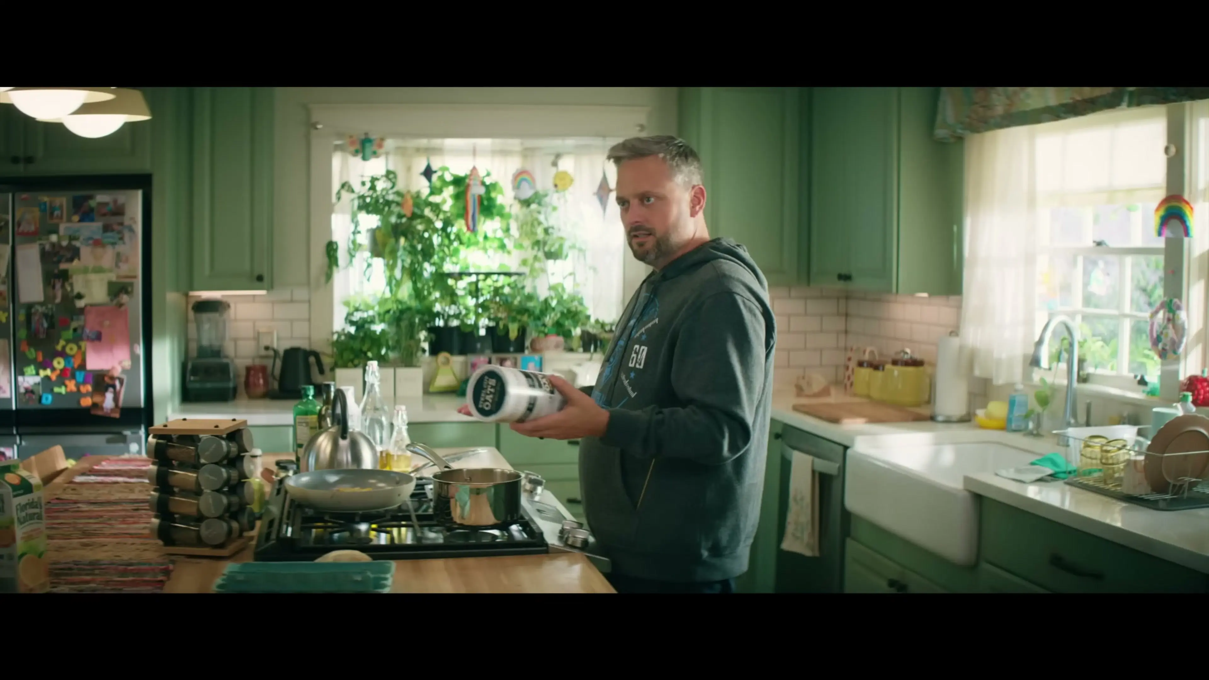 Nate holds a container beside the stove in a green kitchen.