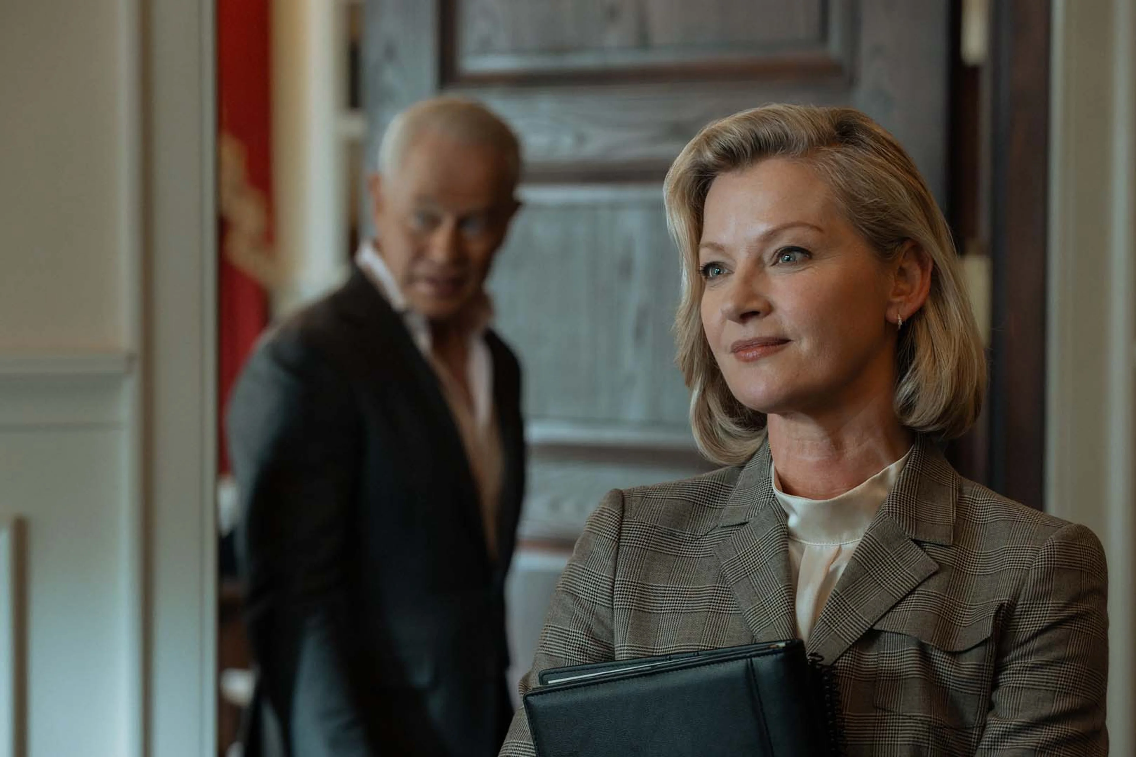 Gretchen Mol as Amanda Clark stands in the foreground while Neal McDonough as Cal Thresher watches from a doorway.