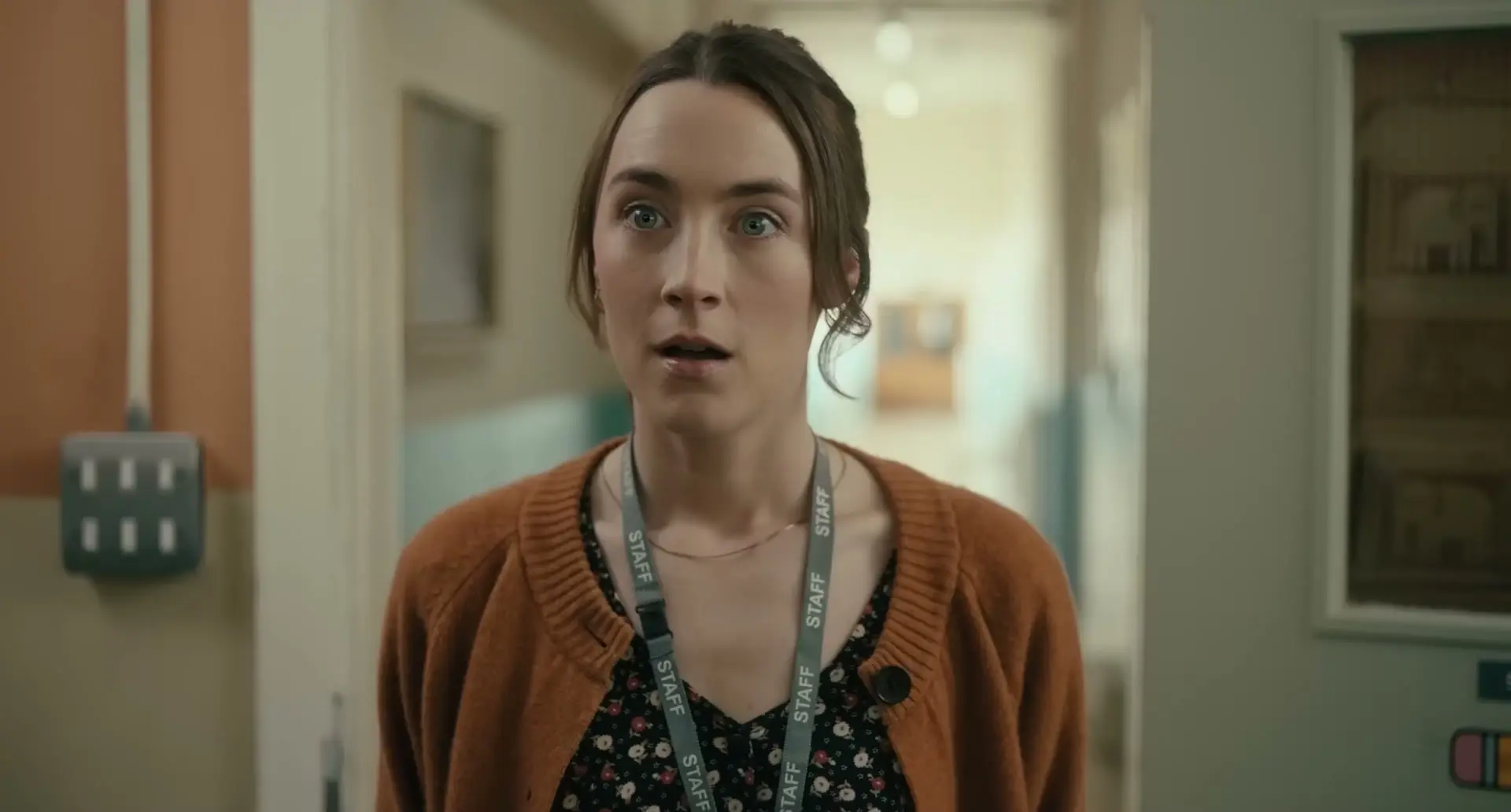 Saoirse Ronan as teacher Maria looks stunned in a bright school corridor.
