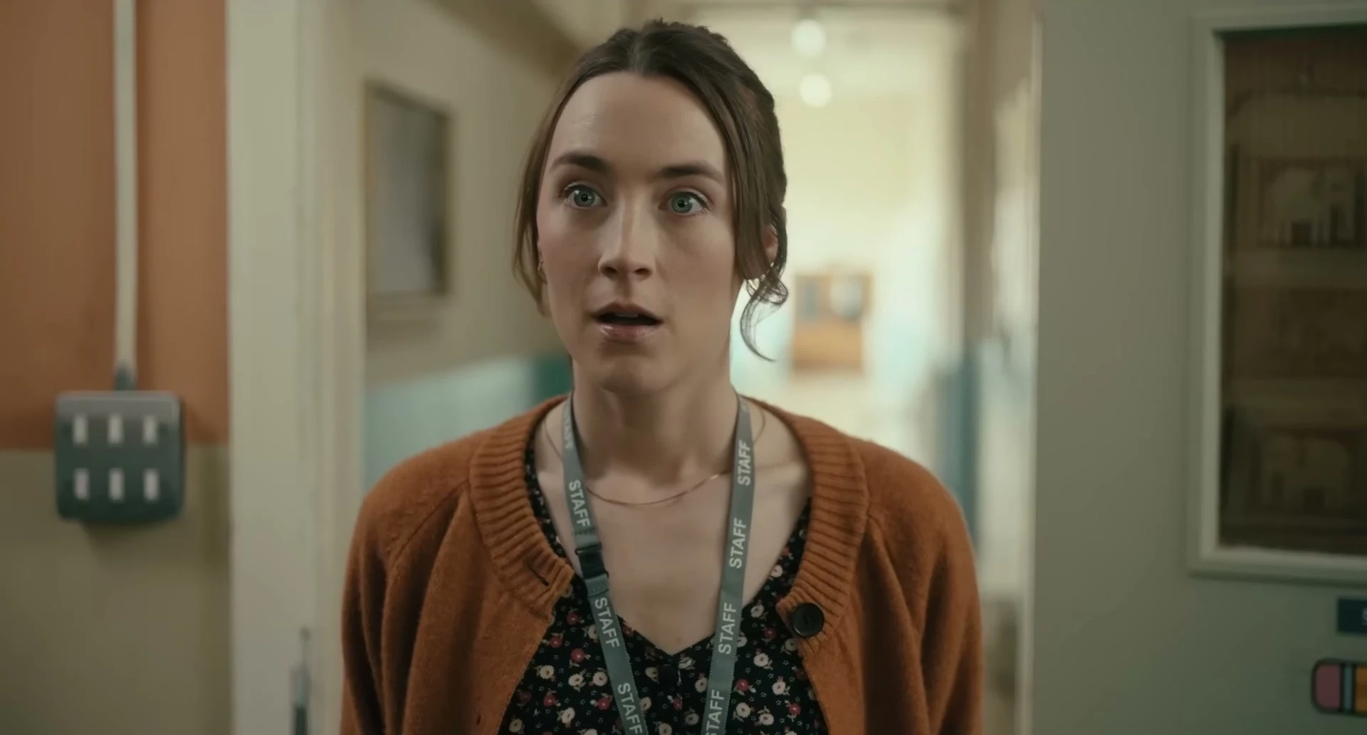 Saoirse Ronan as teacher Maria looks stunned in a bright school corridor.