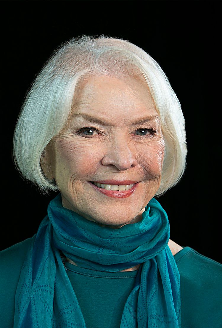 Ellen Burstyn smiles in a teal scarf against a dark background.
