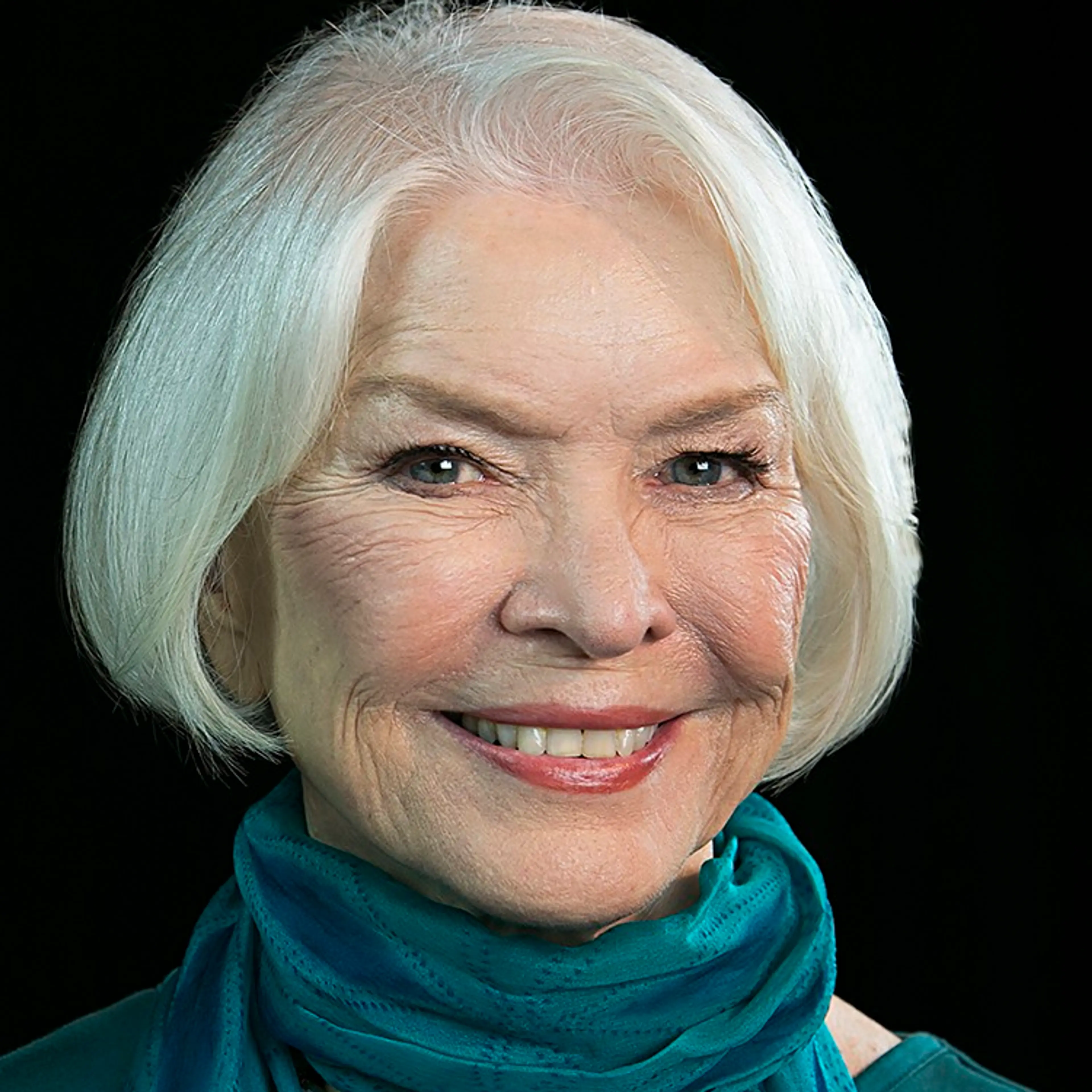 Ellen Burstyn smiles in a teal scarf against a dark background.