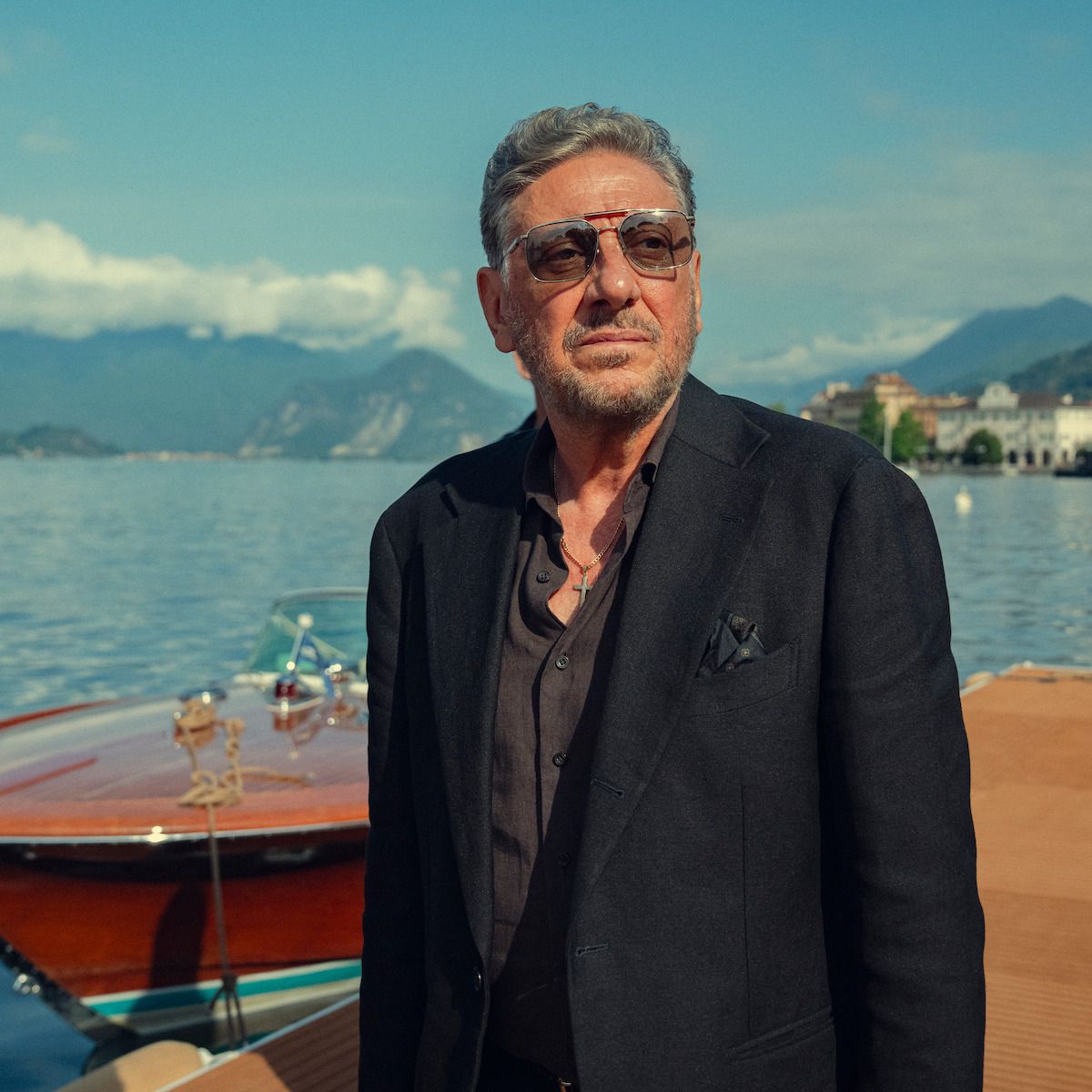 Sergio Castellitto as Marco Moretti standing by a wooden boat on a lakeside dock.