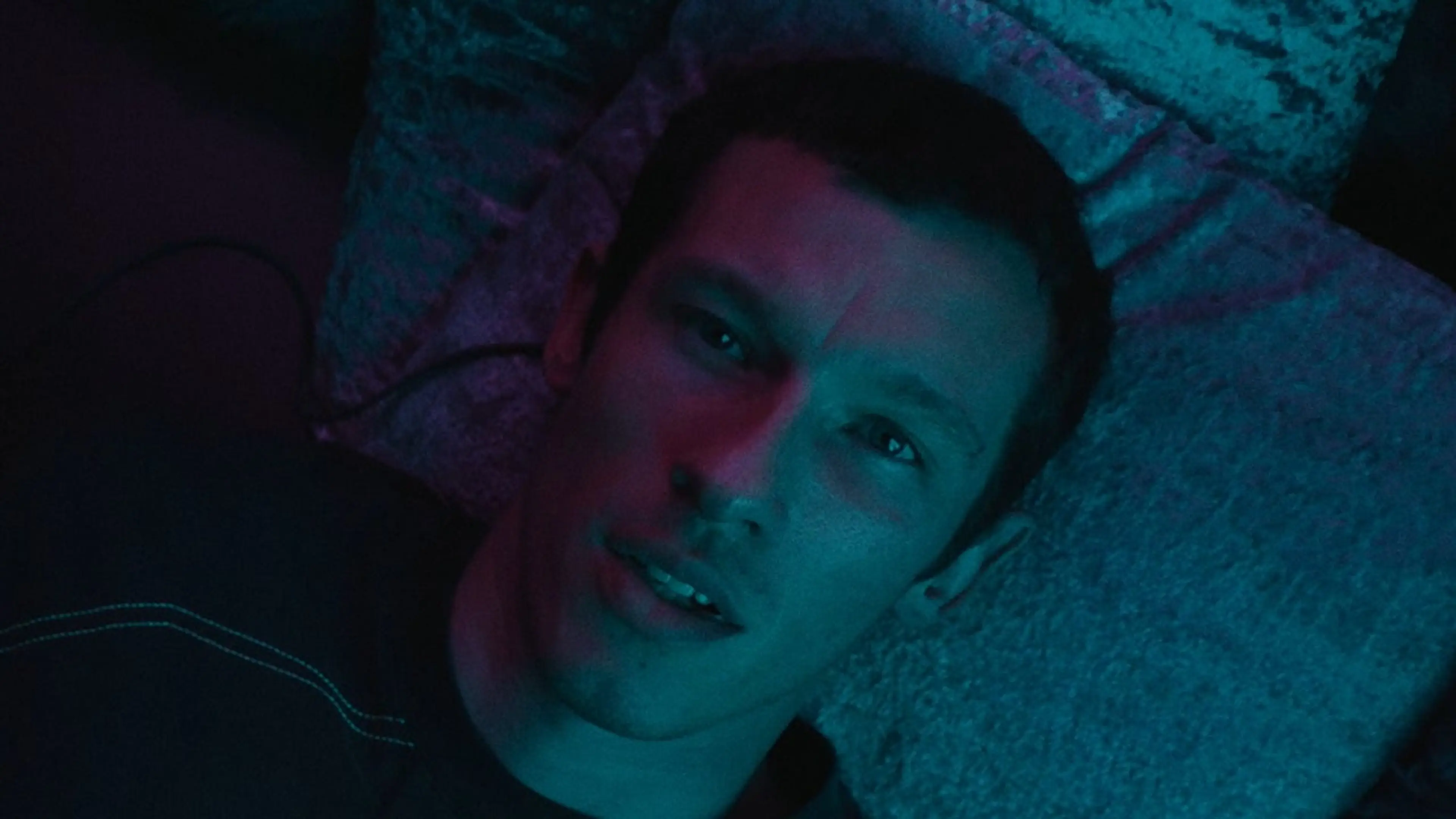 Callum Turner as Case lying under blue and pink light in Neuromancer.
