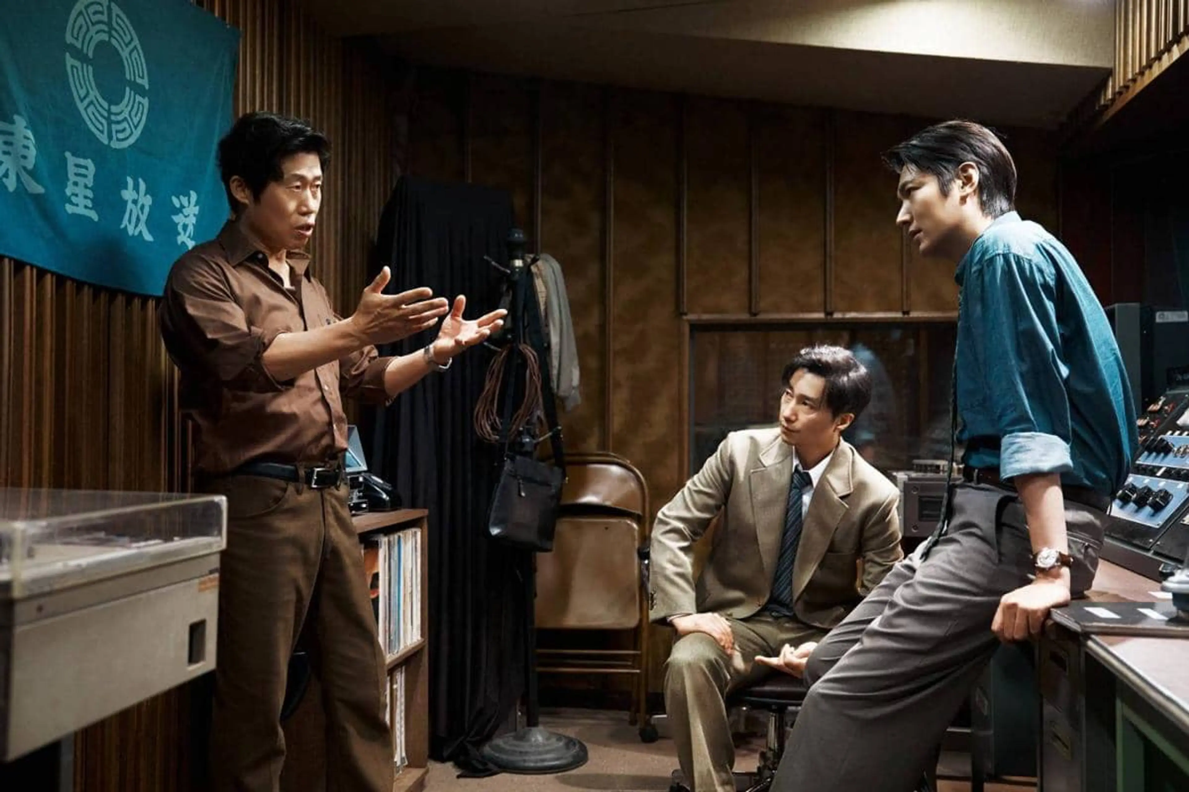 Three men talk in a 1970s radio studio in an official still from The Assassin(s).