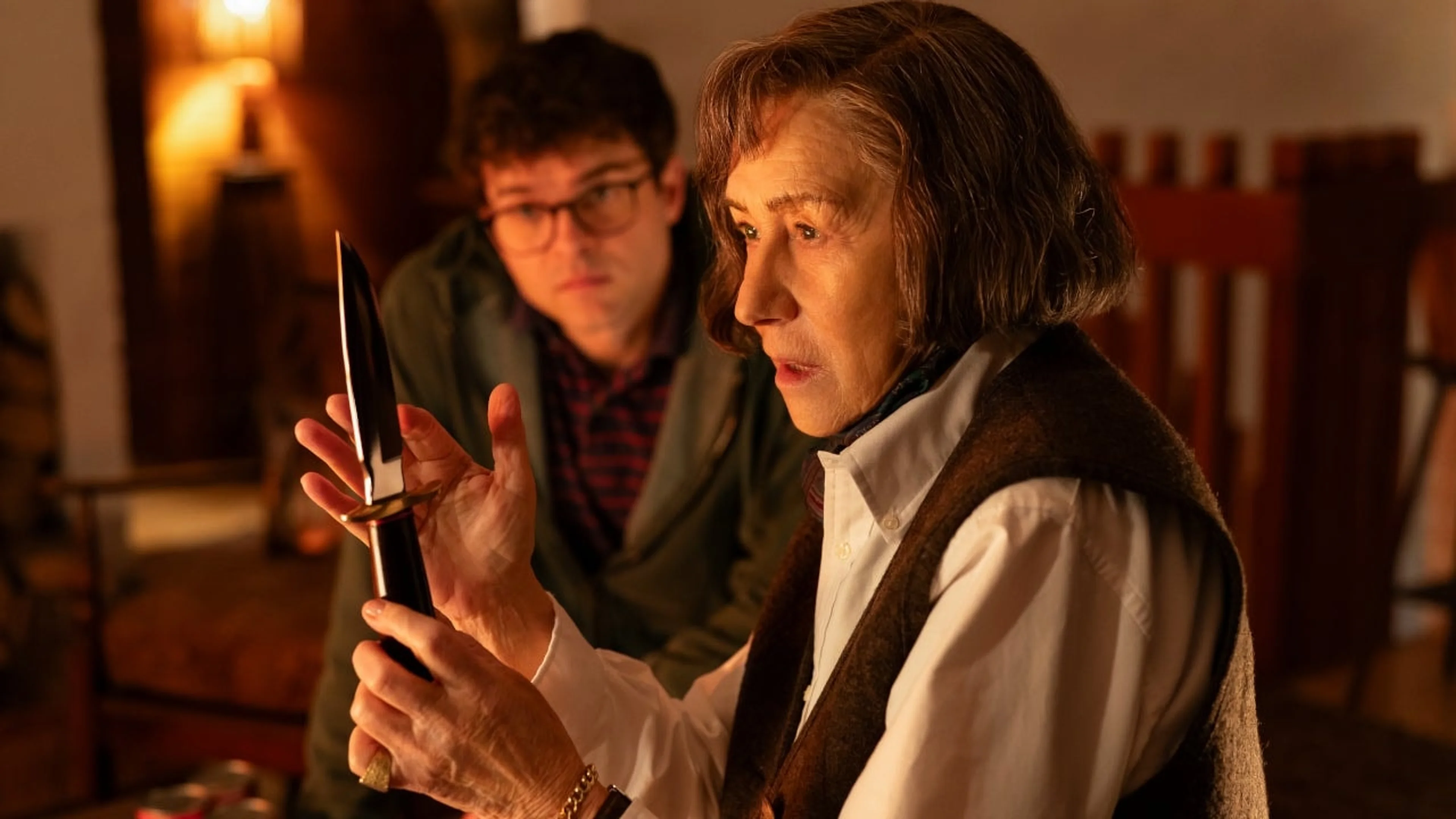 Helen Mirren examines a knife while Alden Ehrenreich stands behind her in a film still.