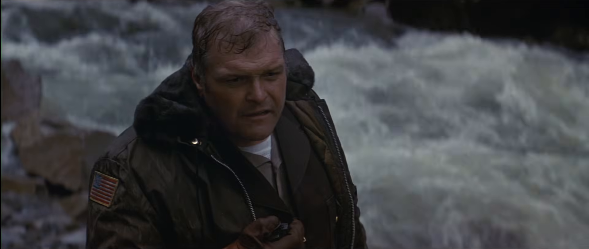 A uniformed officer struggles in rushing river water during the pursuit in First Blood.