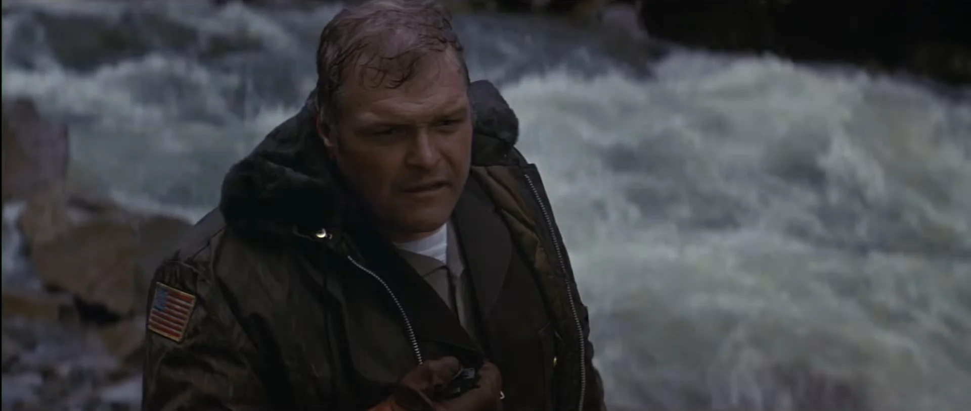 A uniformed officer struggles in rushing river water during the pursuit in First Blood.