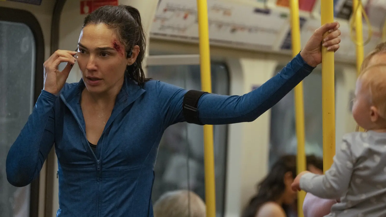 Gal Gadot as Maia Marten speaks through an earpiece while standing injured on a London Underground train in The Runner.