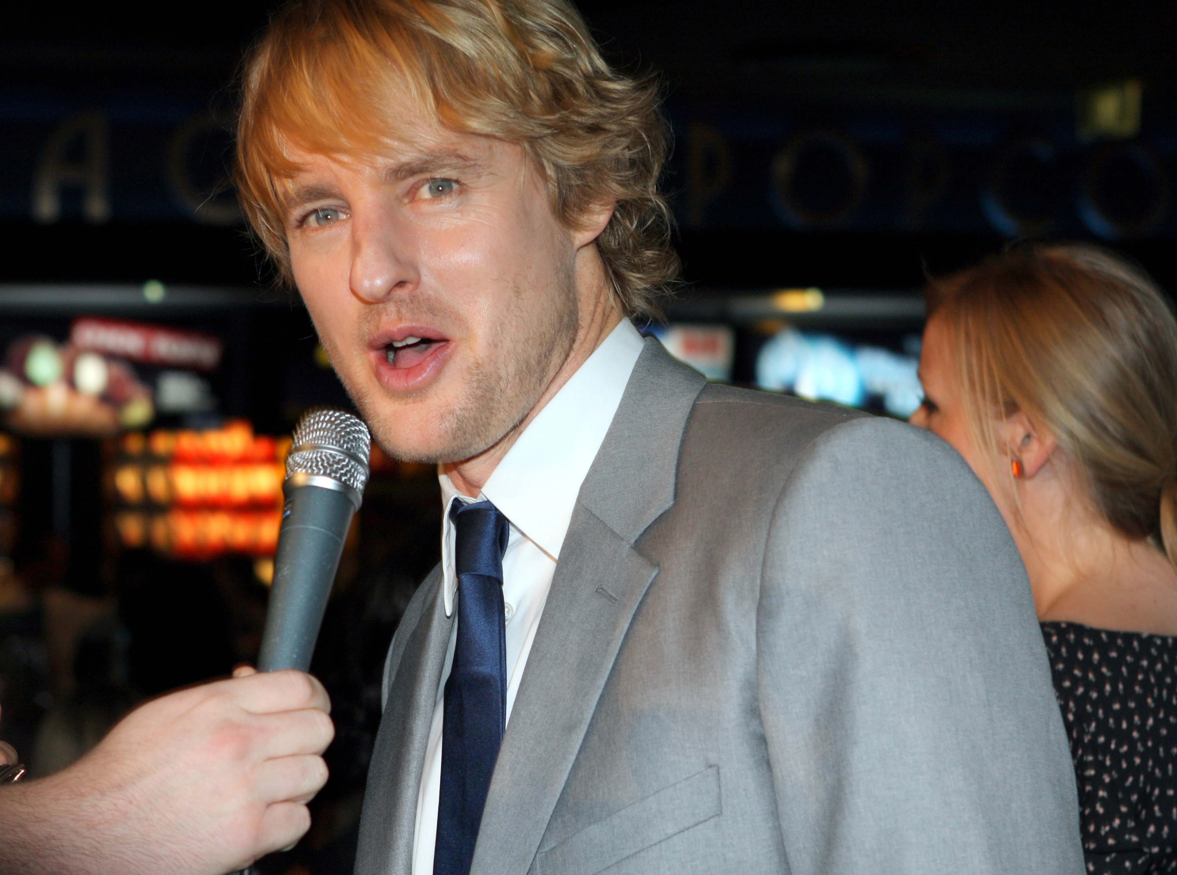Owen Wilson holds a microphone and wears a grey suit at the Hall Pass red carpet in 2011.