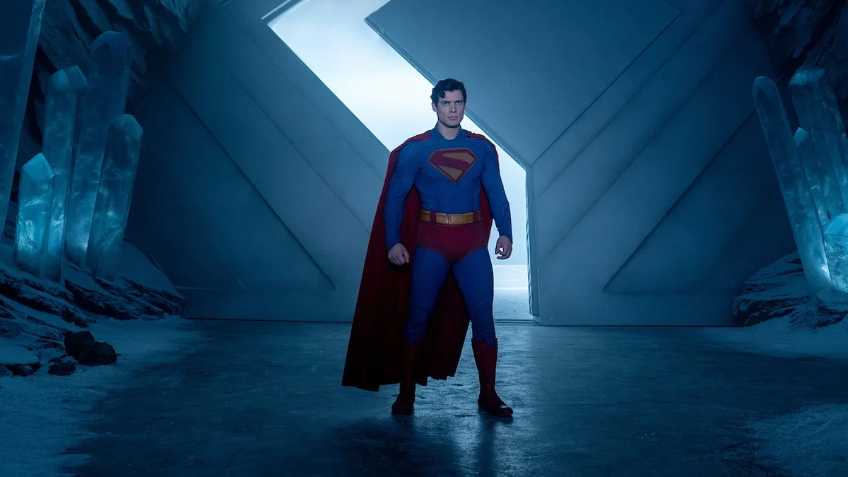 Superman stands in a blue-lit interior in an official DC still from the 2025 film.