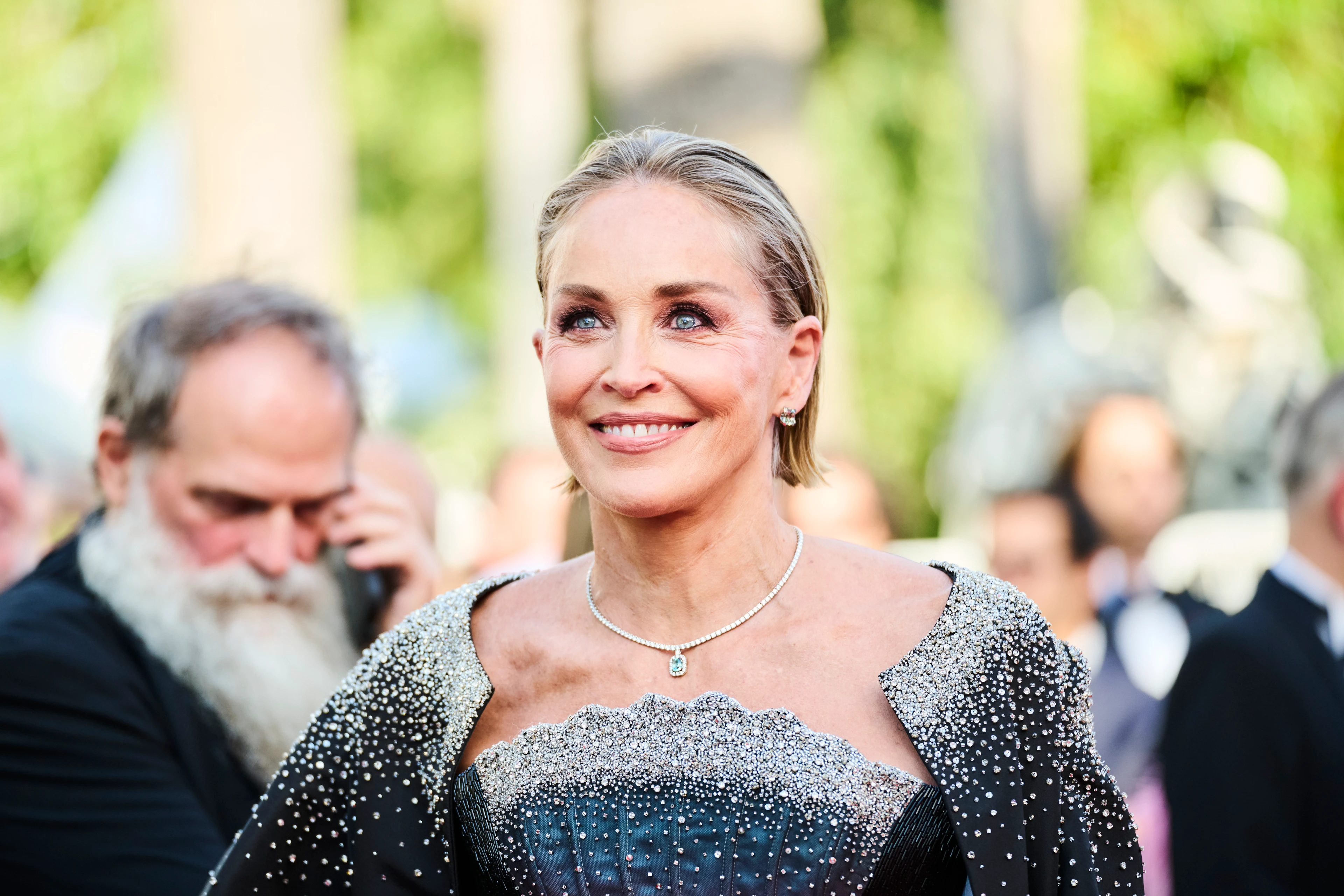 Sharon Stone smiles on the Cannes red carpet in a sparkling black-and-silver outfit.