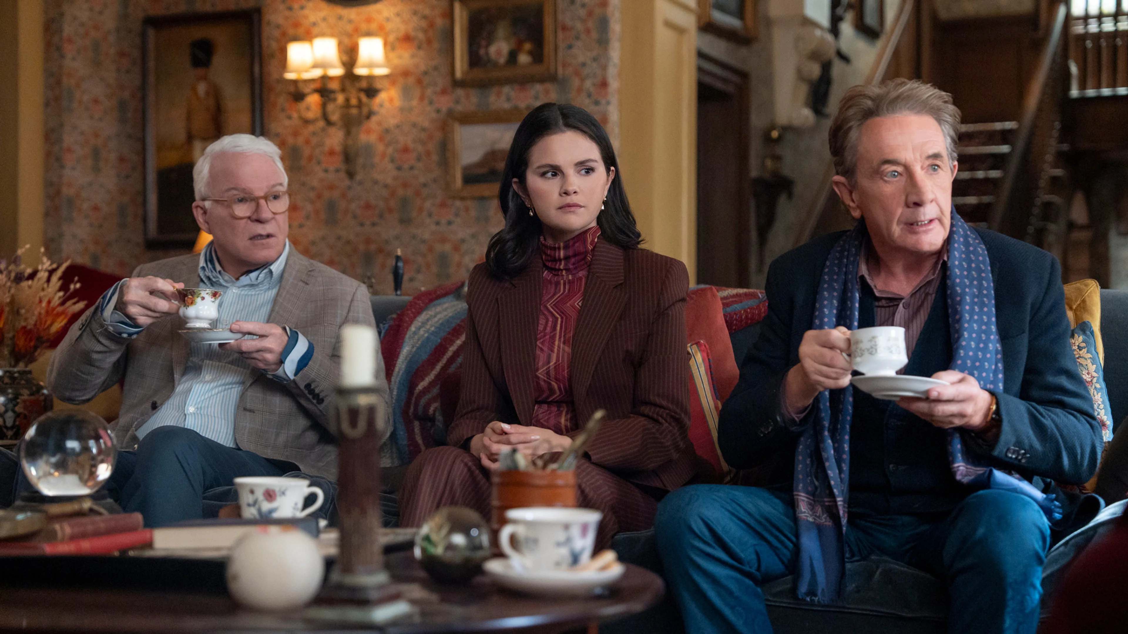 Charles, Mabel, and Oliver sit together inside a richly decorated London room in an official Only Murders in the Building Season 6 still.