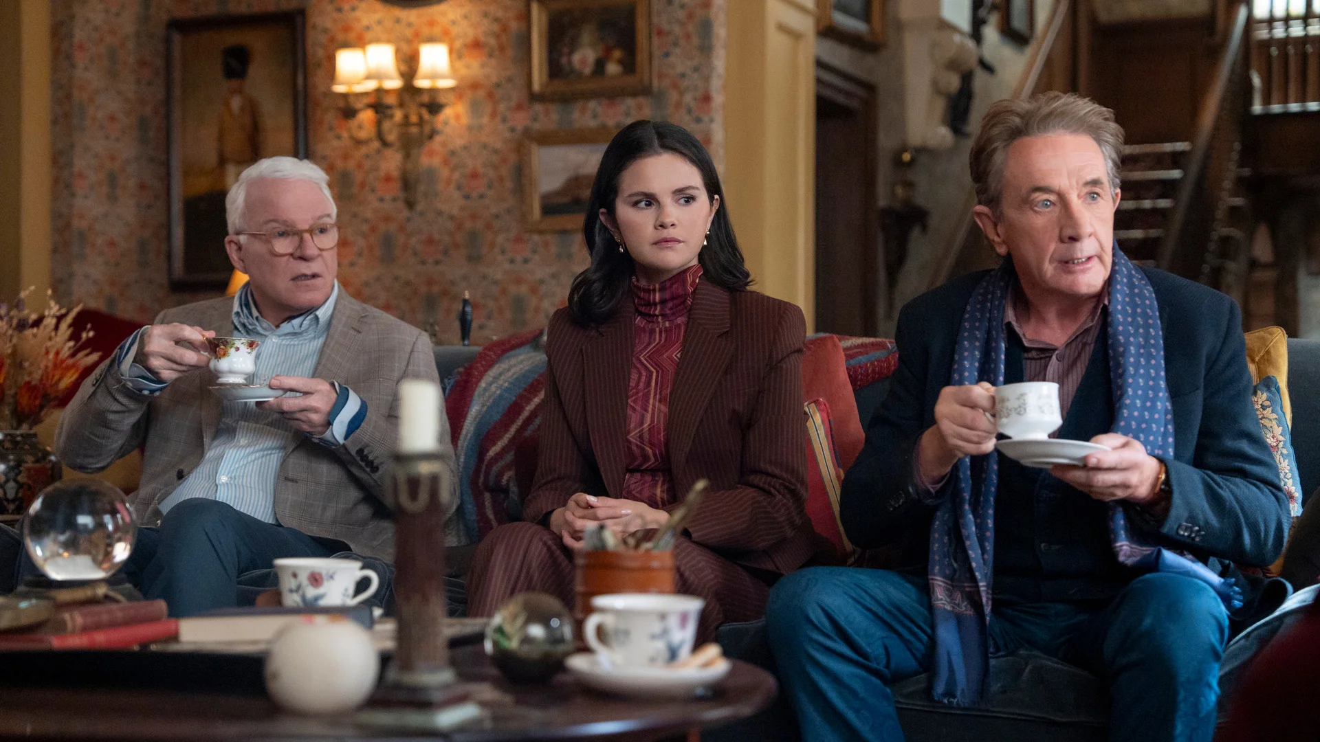 Charles, Mabel, and Oliver sit together inside a richly decorated London room in an official Only Murders in the Building Season 6 still.