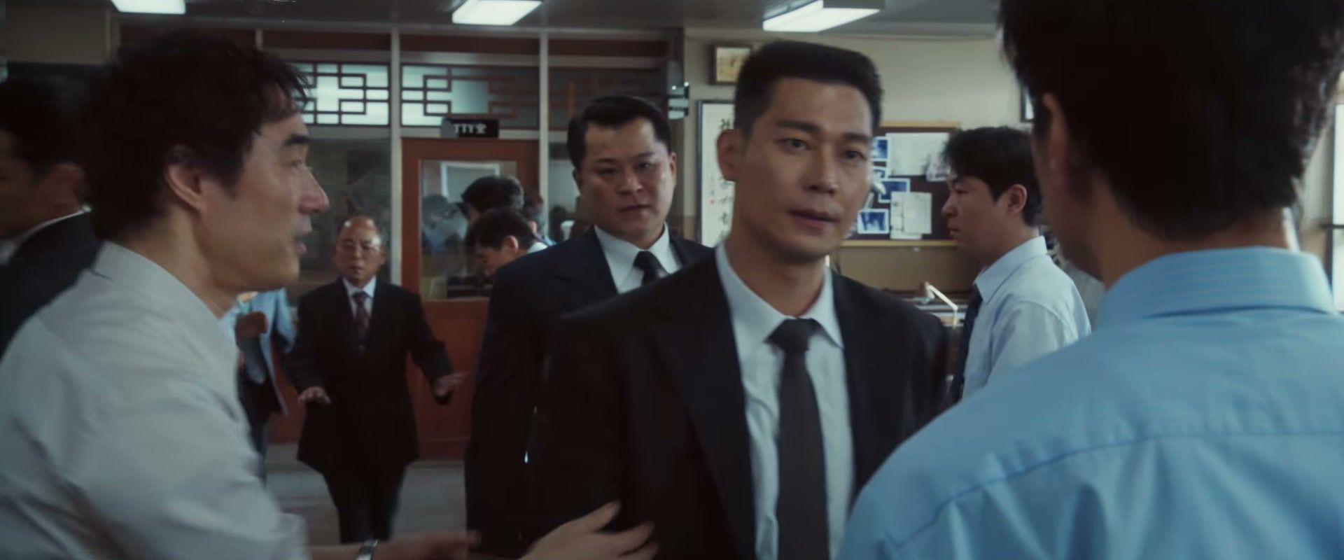 Several men meet in a crowded newsroom.