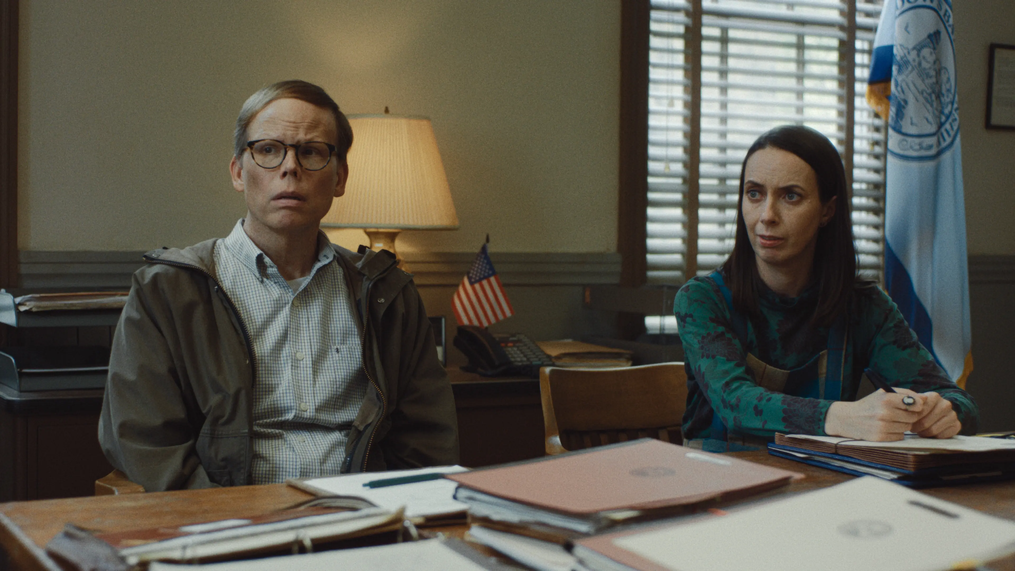 Jeff Hiller and Kate O’Flynn sit at a table in the town office.