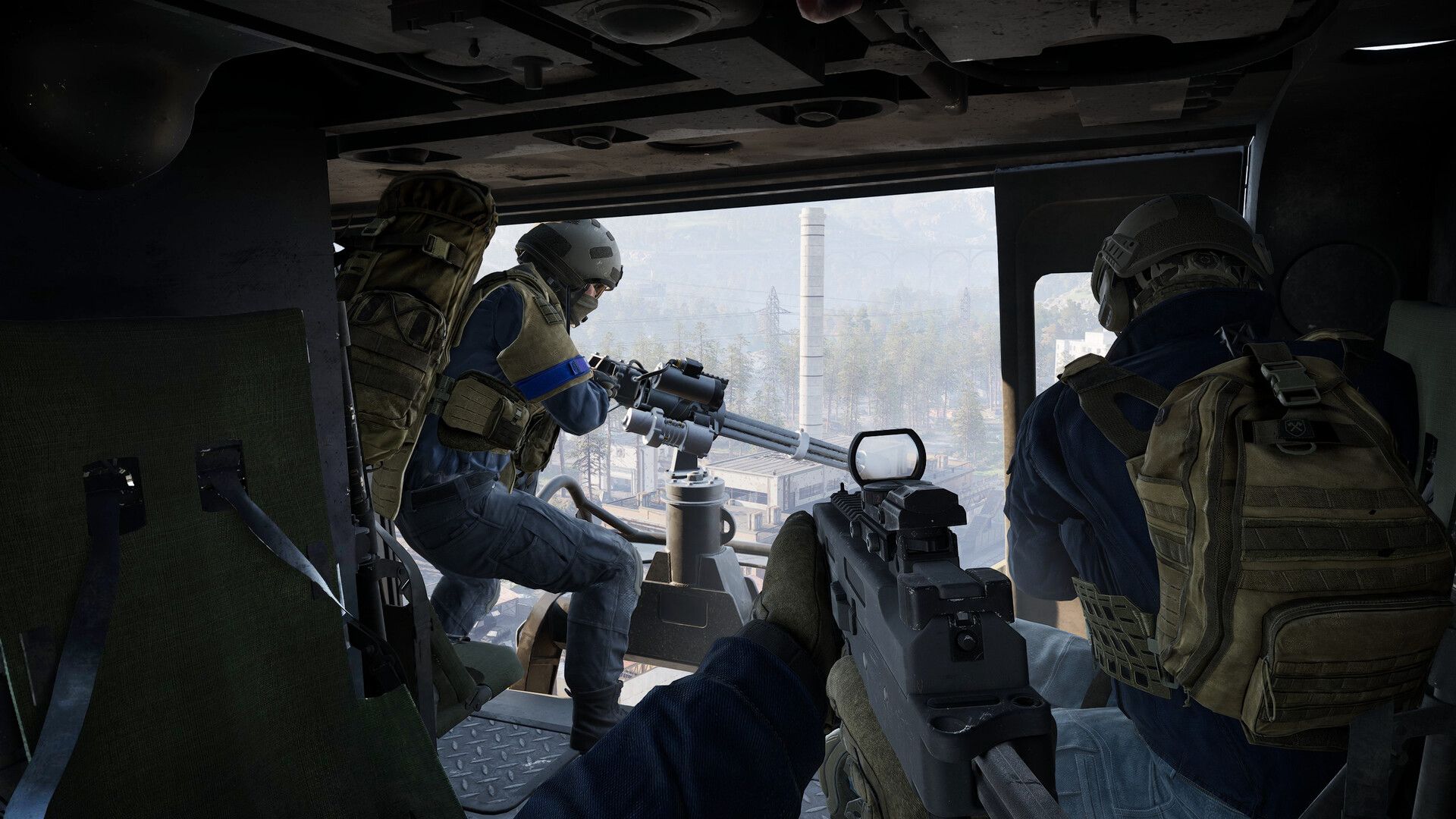 A first-person gunner looks out from a helicopter toward an industrial city with two teammates in WARDOGS.