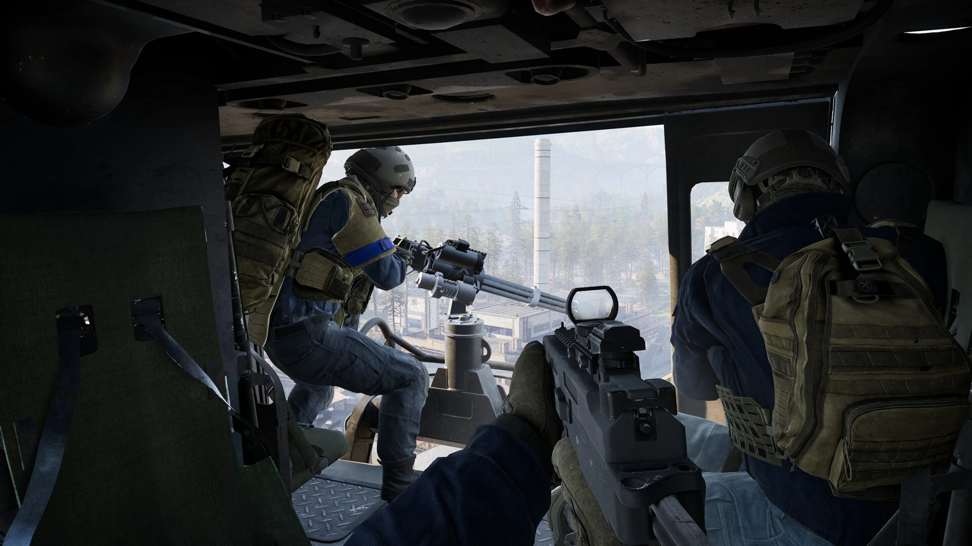 Two soldiers ride inside a WARDOGS helicopter above an industrial city; one operates its mounted gun.