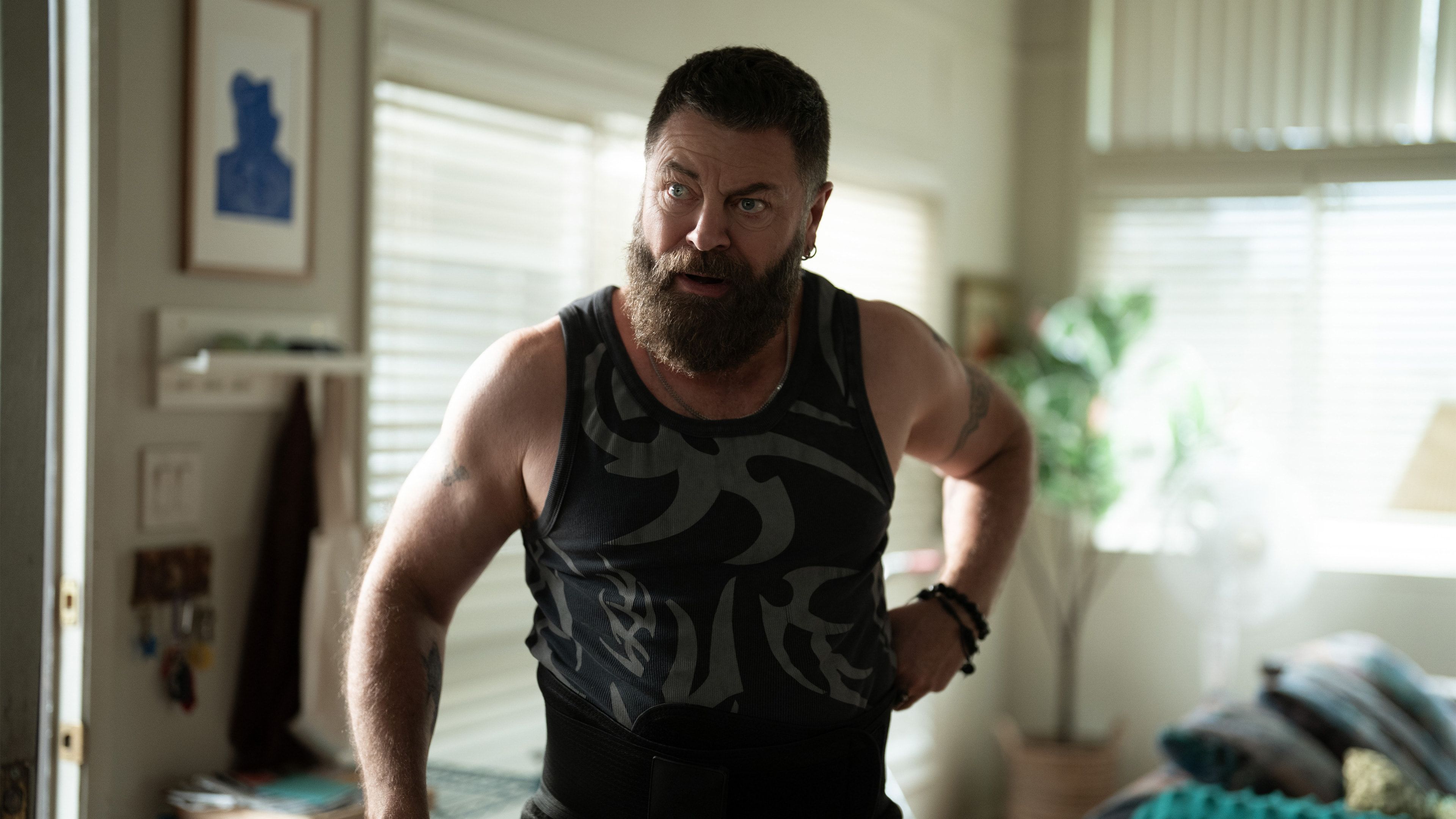 Nick Offerman as Jinx stands indoors wearing a camouflage tank top.