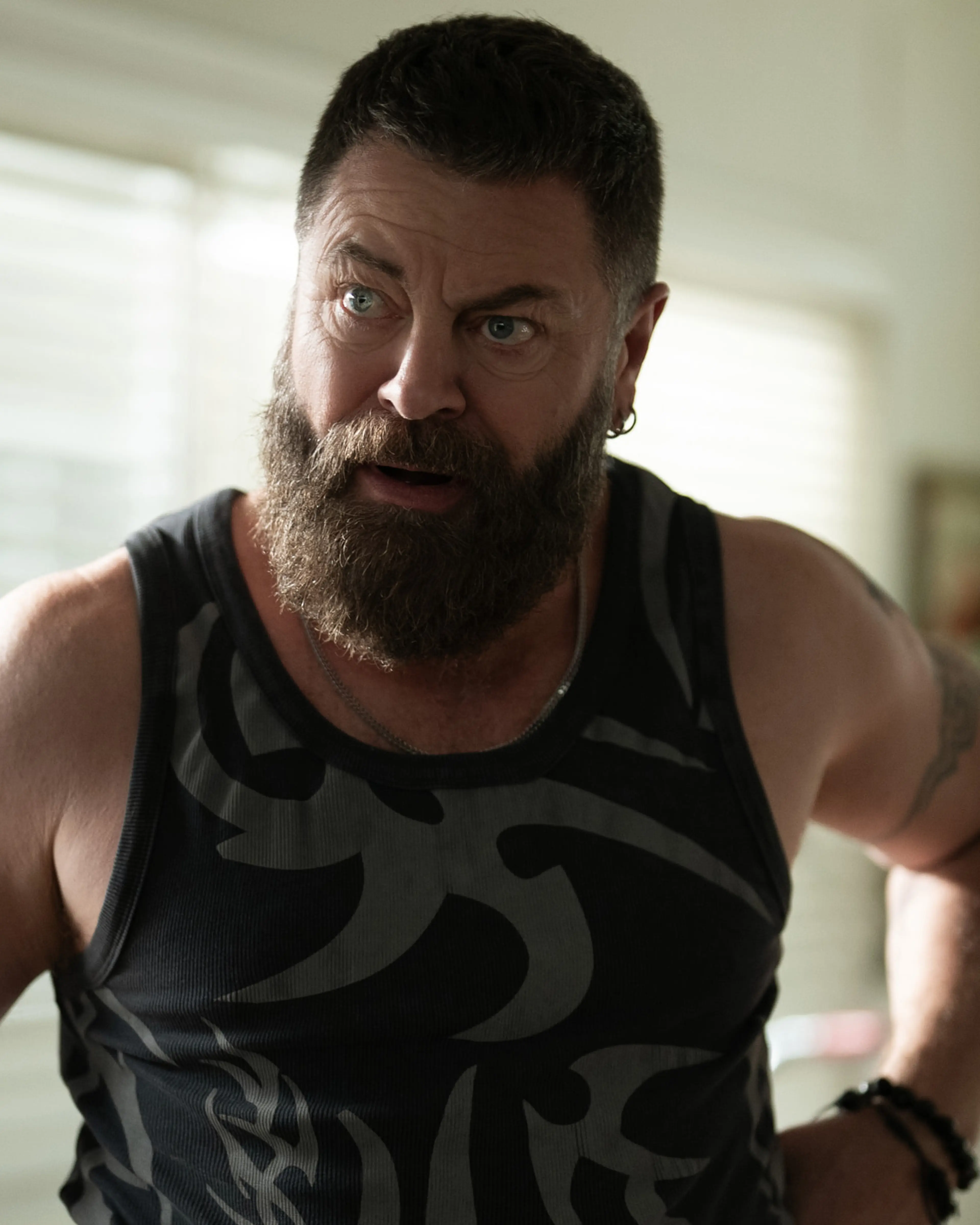 Nick Offerman as Jinx stands indoors wearing a camouflage tank top.