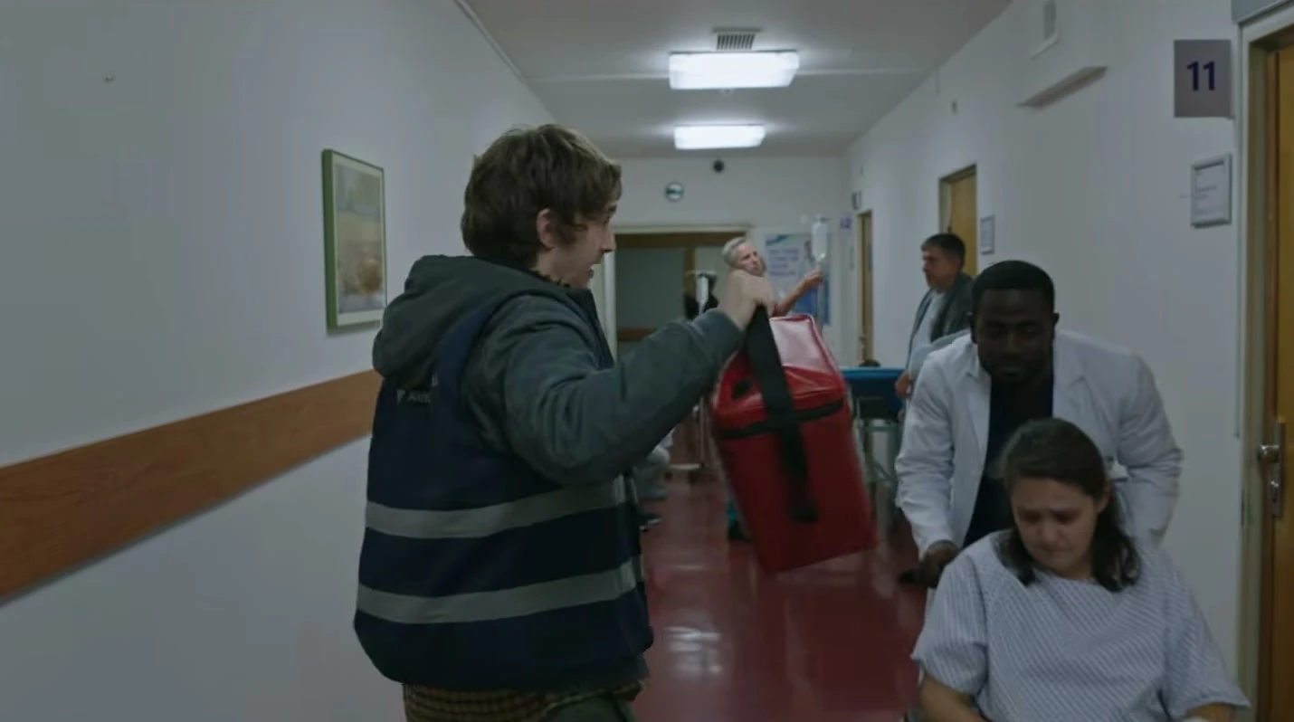 Austin Abrams as courier Bryan walks through a bright medical corridor in Resident Evil.