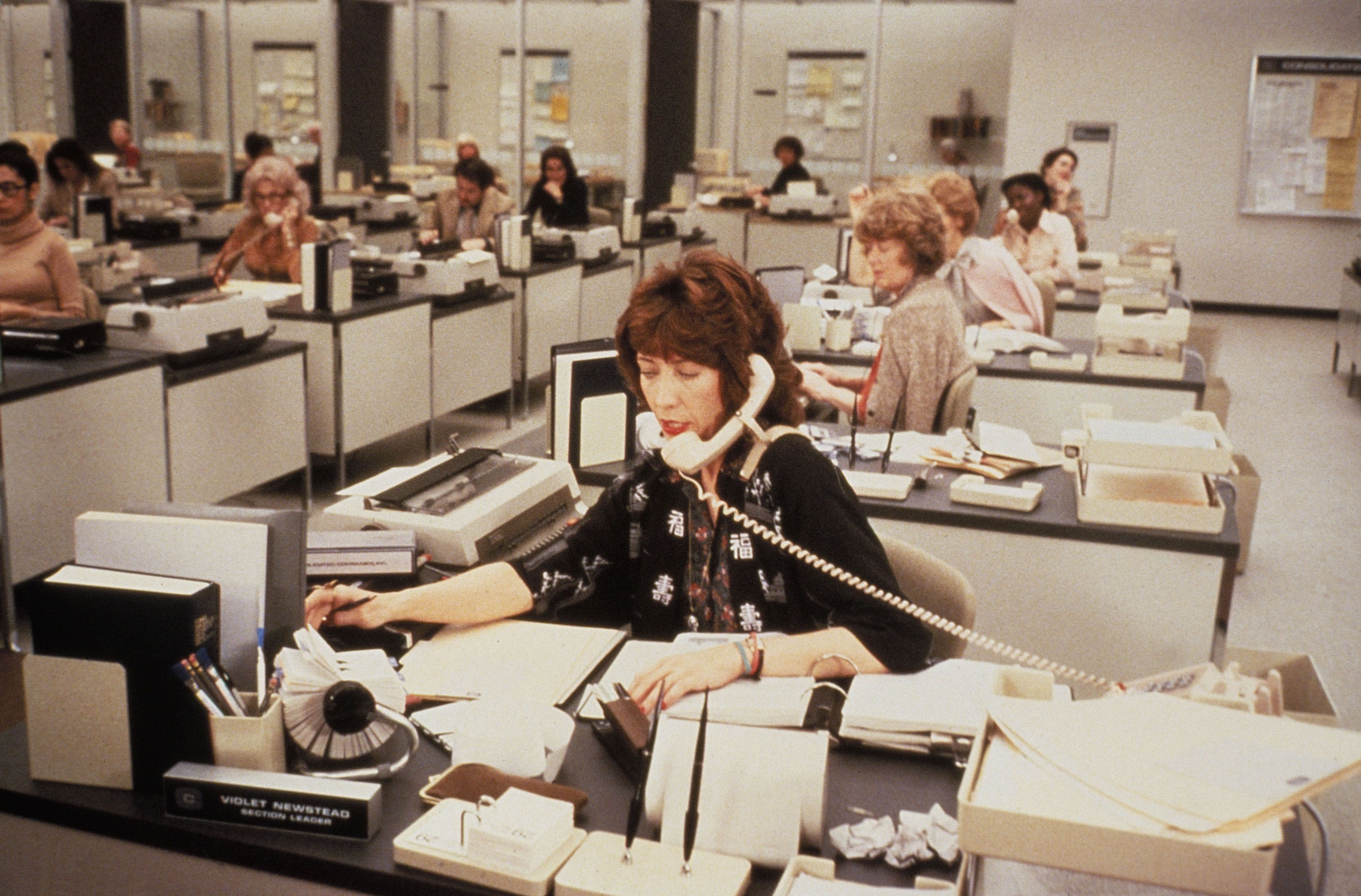 Lily Tomlin at her desk in a busy office scene from 9 to 5.