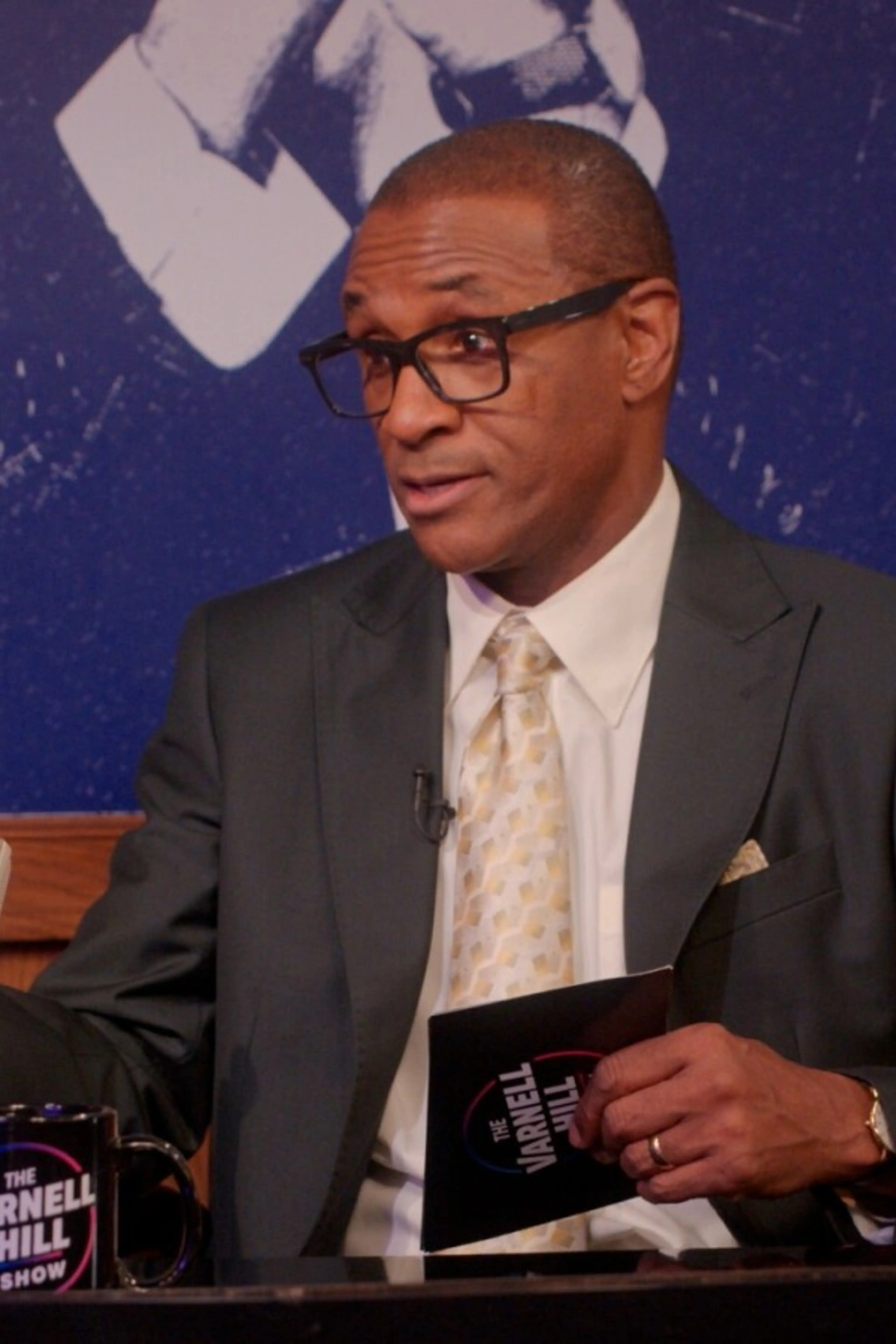 Tommy Davidson appears as Varnell Hill behind a talk-show desk in an official Paramount+ still.