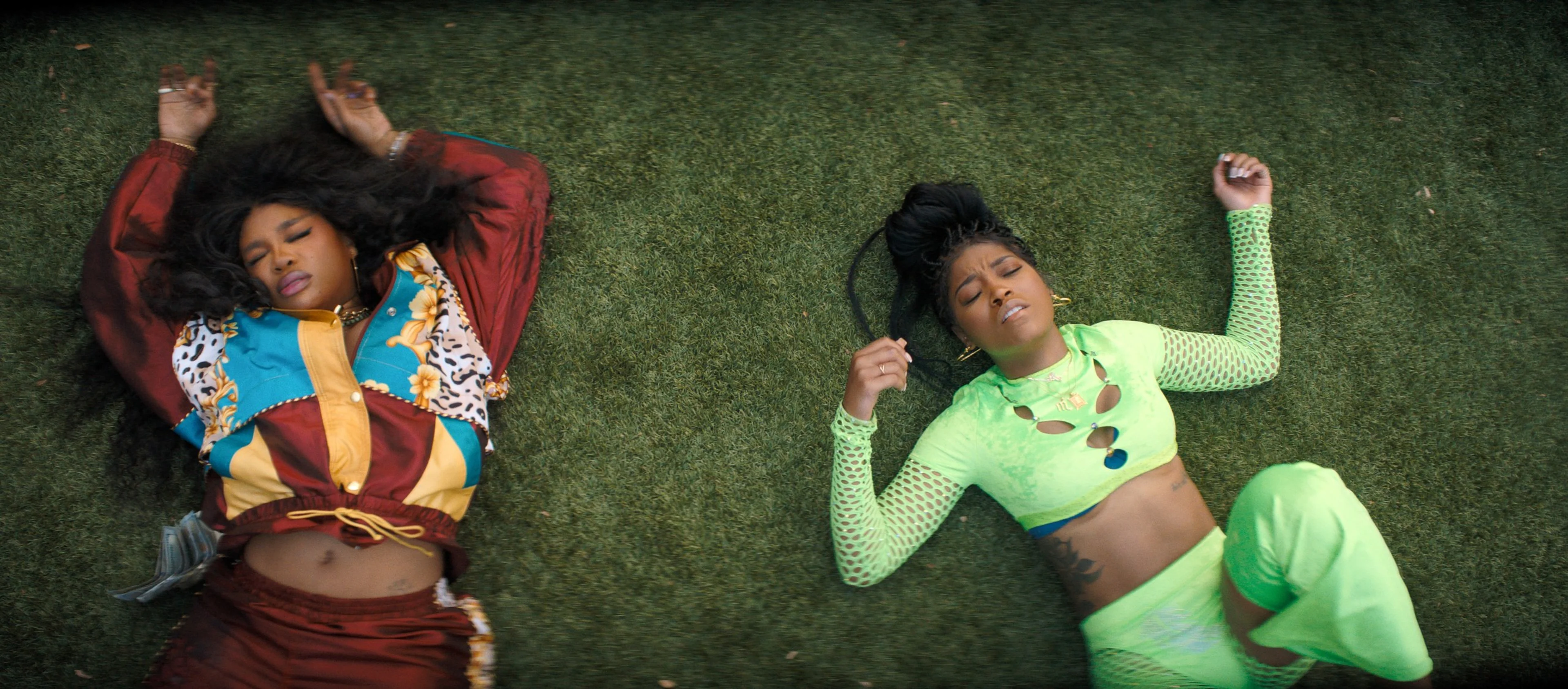 SZA and Keke Palmer lie on the grass with their arms raised beside their heads.