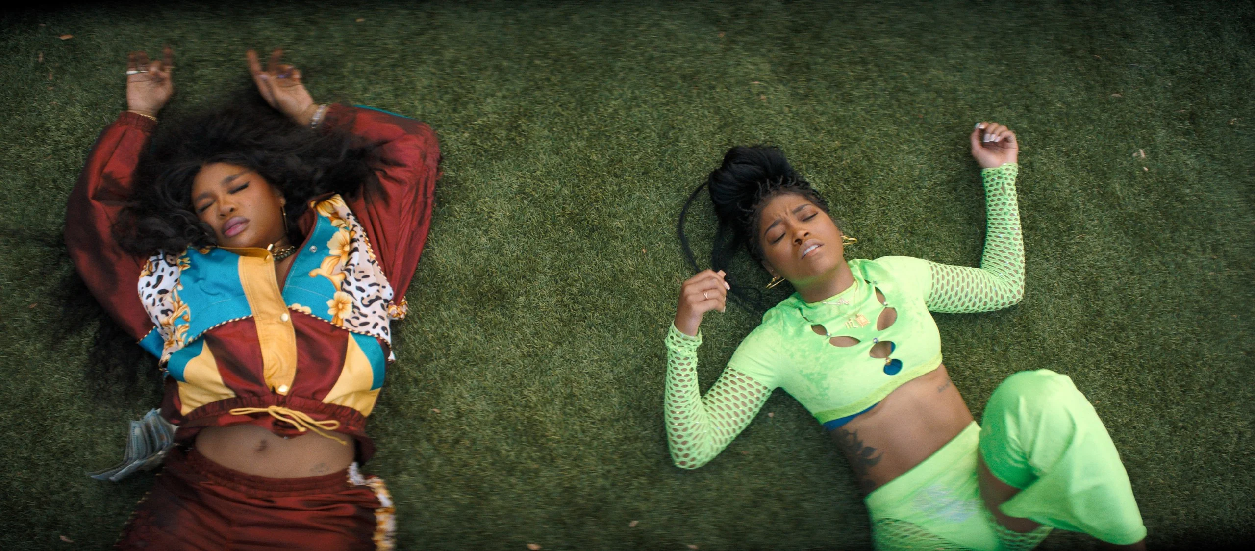 SZA and Keke Palmer lie on the grass with their arms raised beside their heads.