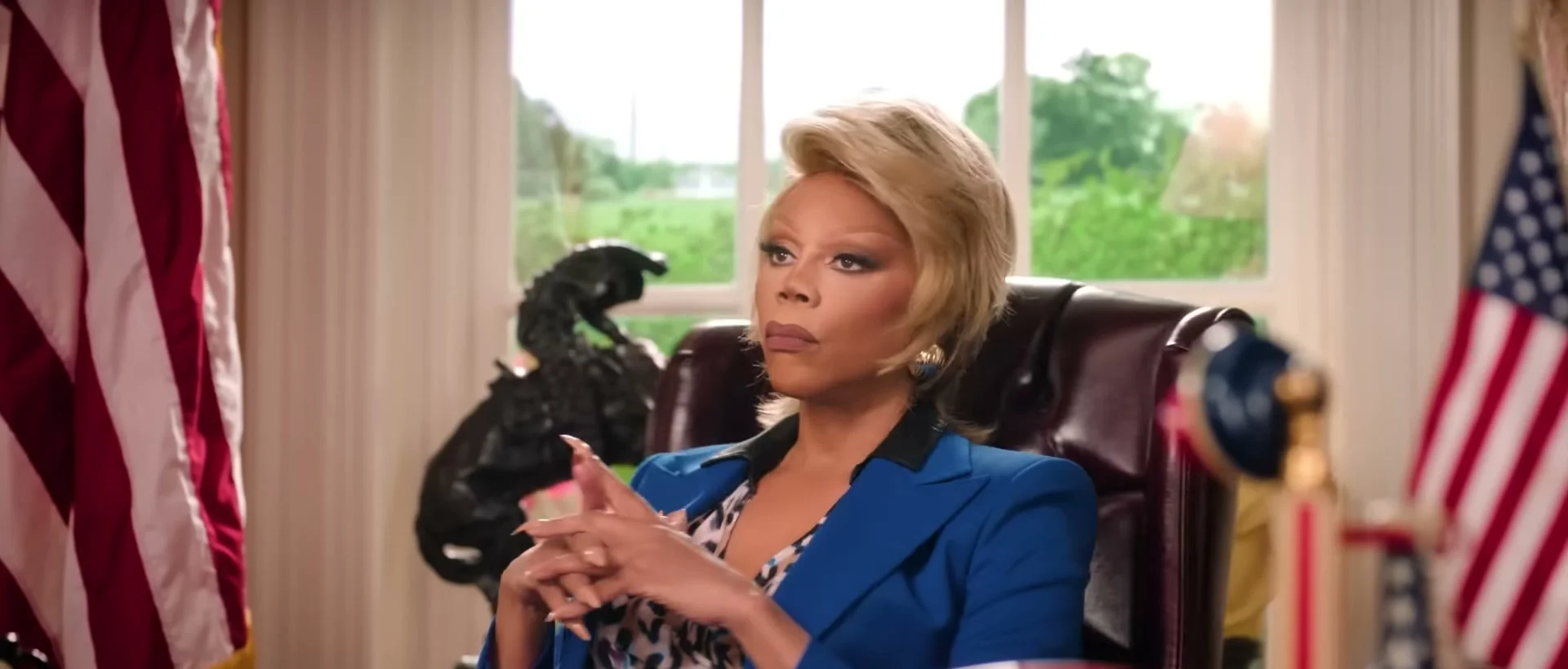 RuPaul as President Judy Gagwell sits behind a desk in Stop! That! Train!.