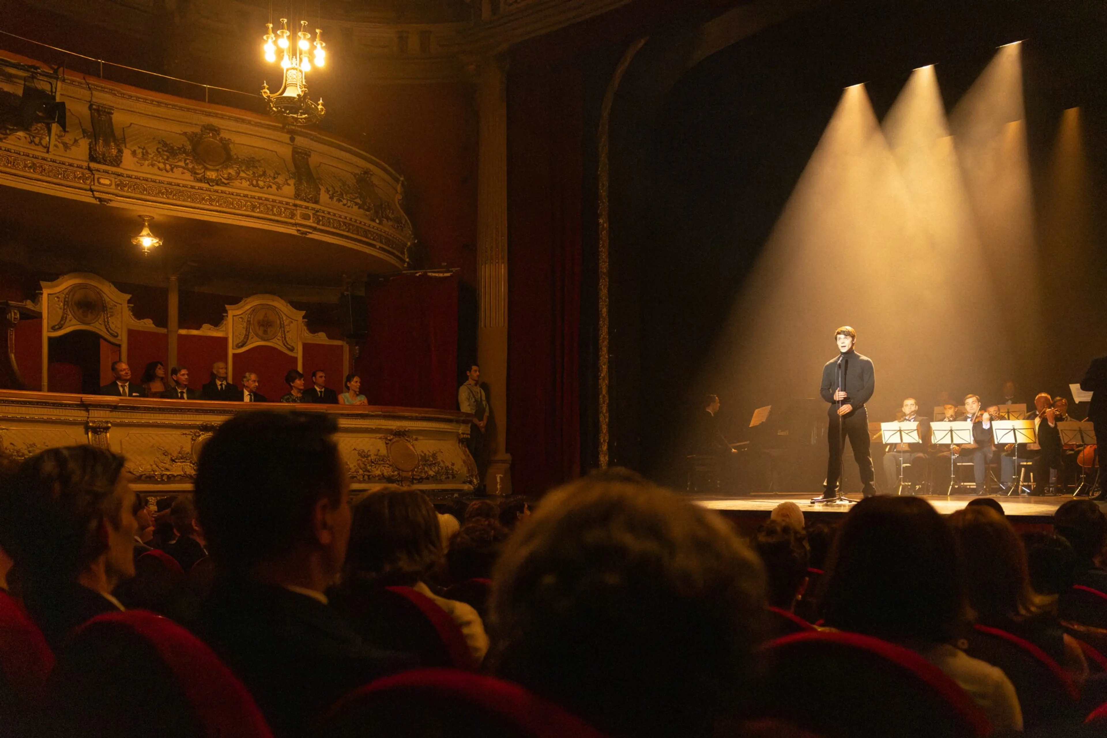 A singer stands under spotlights before an orchestra and theater audience in A Day Like No Other.