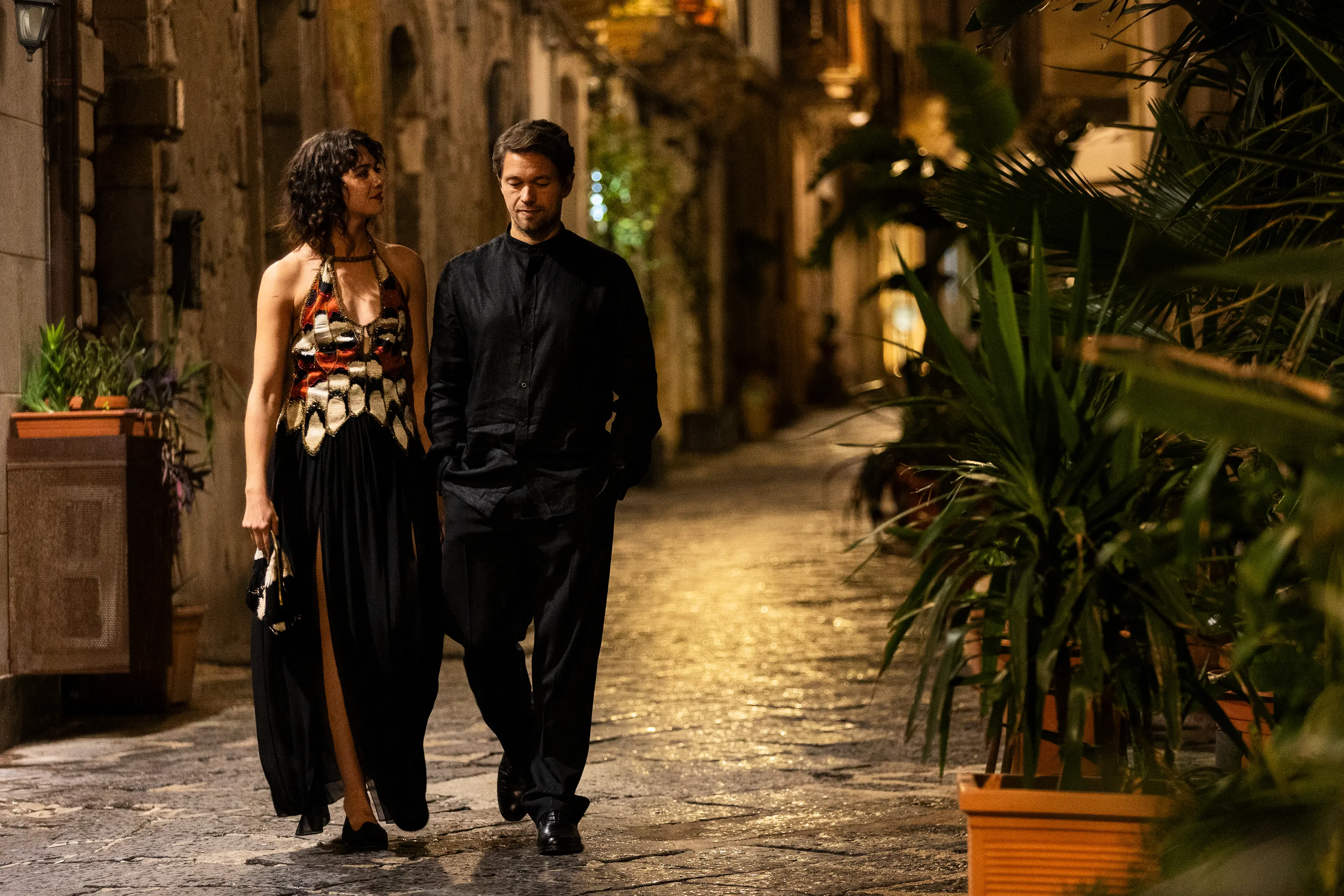 A couple walks along a stone street at night in A Couple of Lies.