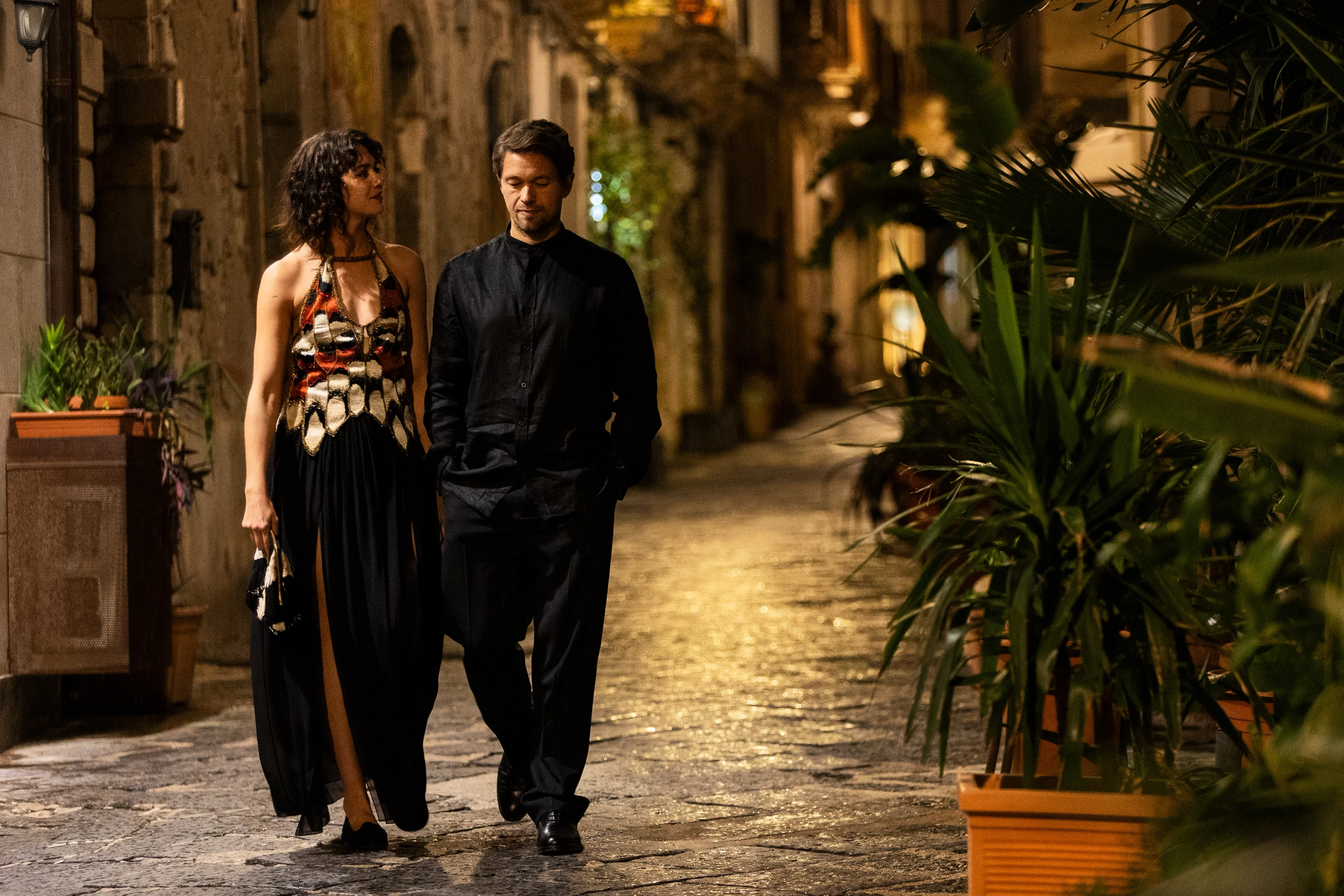 A couple walks along a stone street at night in A Couple of Lies.