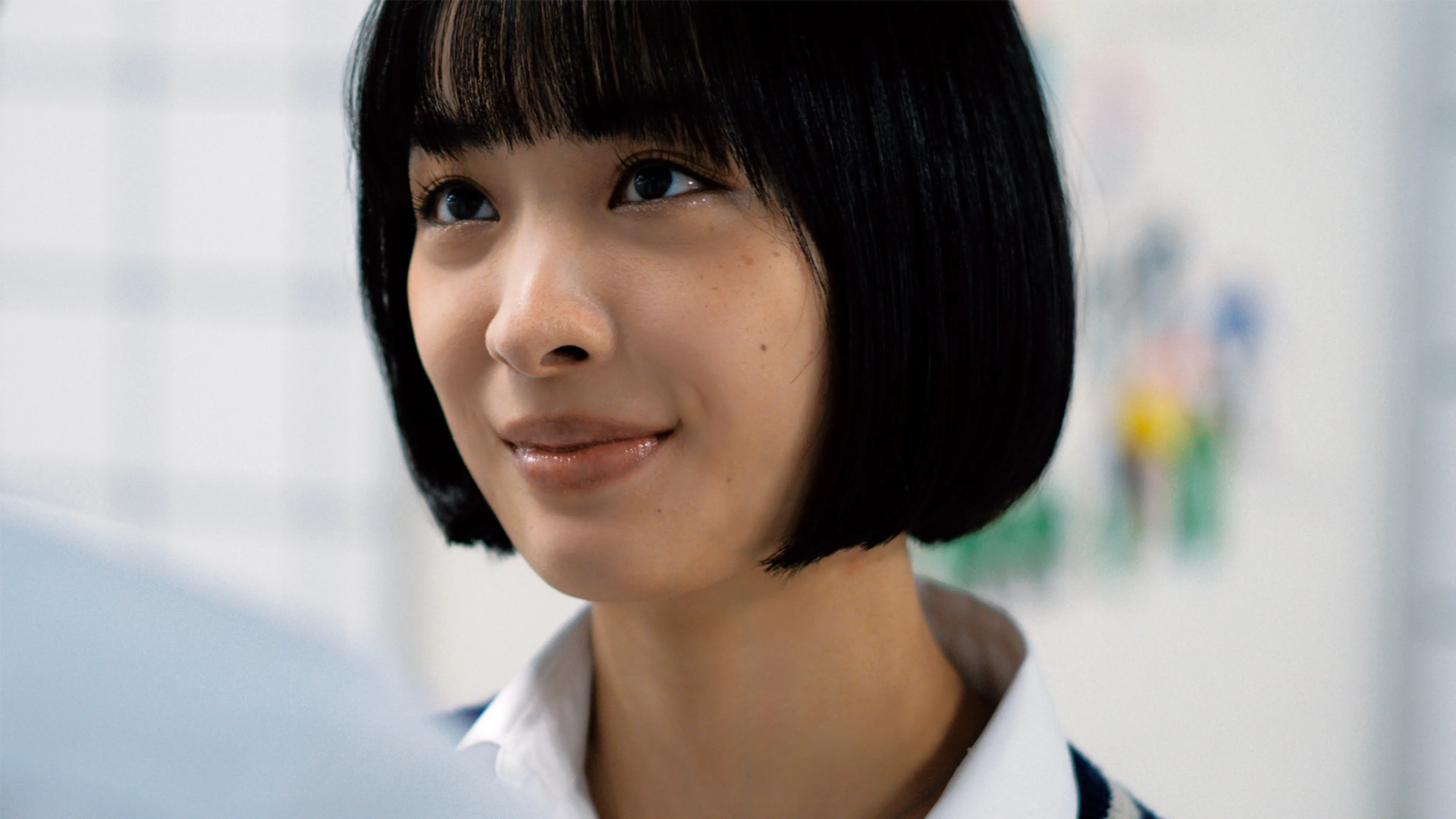 A young woman with a short black bob and a backpack strap looks upward.