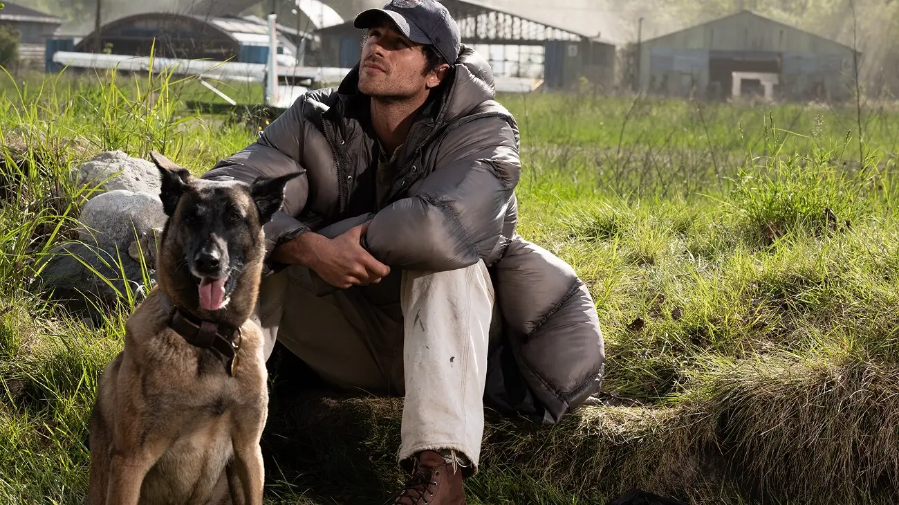 Jacob Elordi as Hig crouches beside his dog Jasper at an airfield in The Dog Stars.