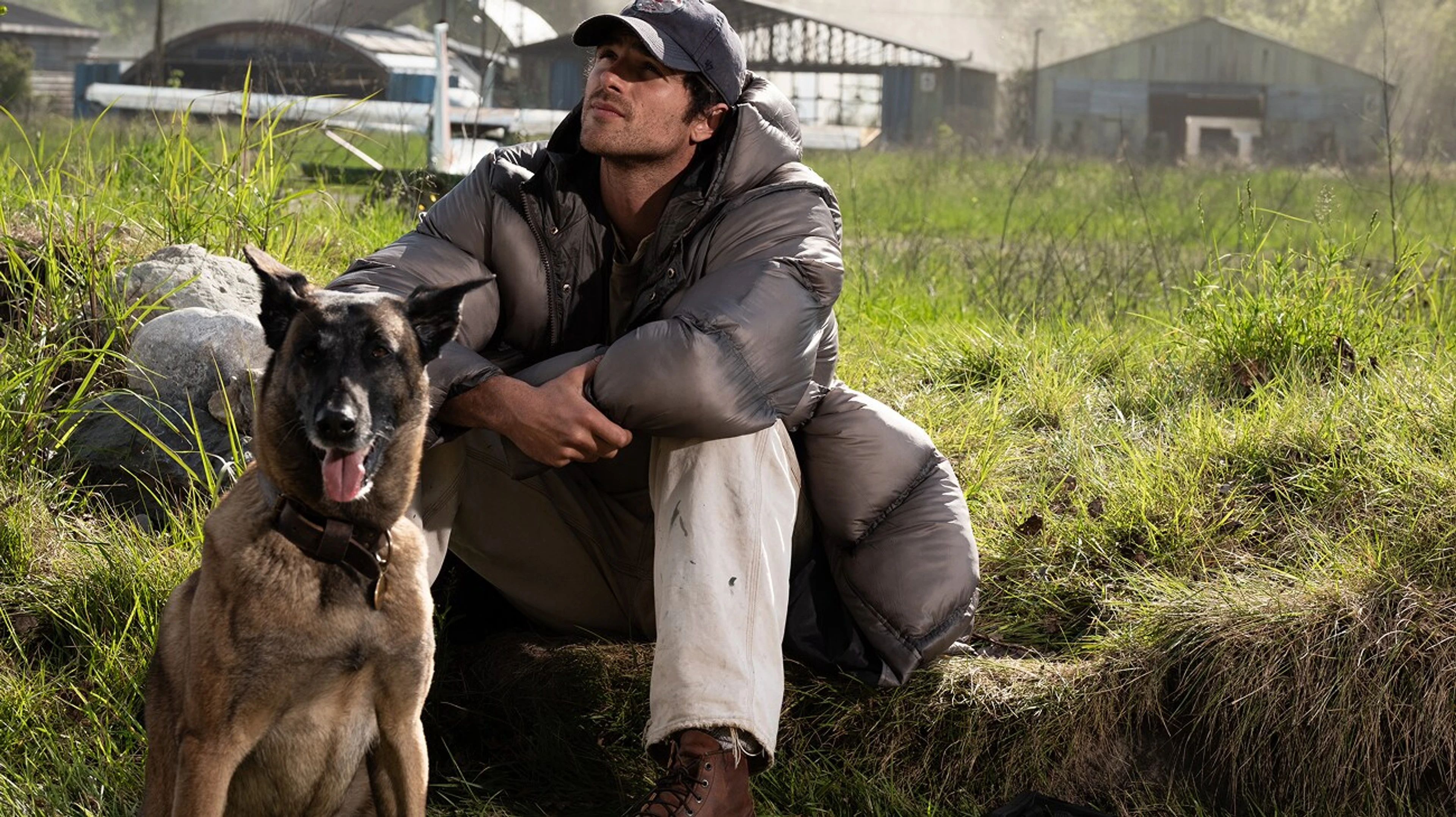Jacob Elordi as Hig crouches beside his dog Jasper at an airfield in The Dog Stars.