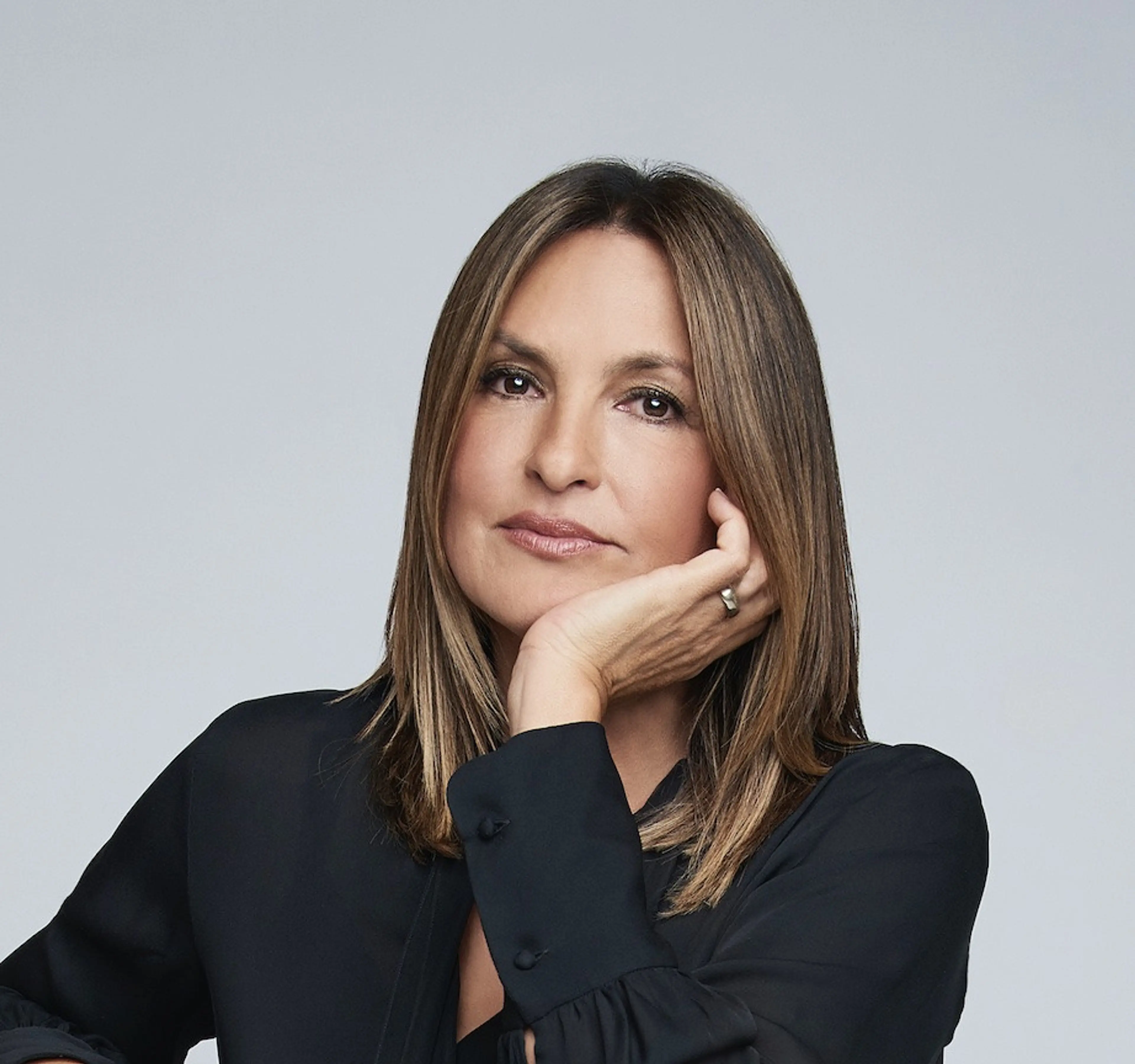 Mariska Hargitay looks toward the camera, resting her face on her hand in a black shirt.
