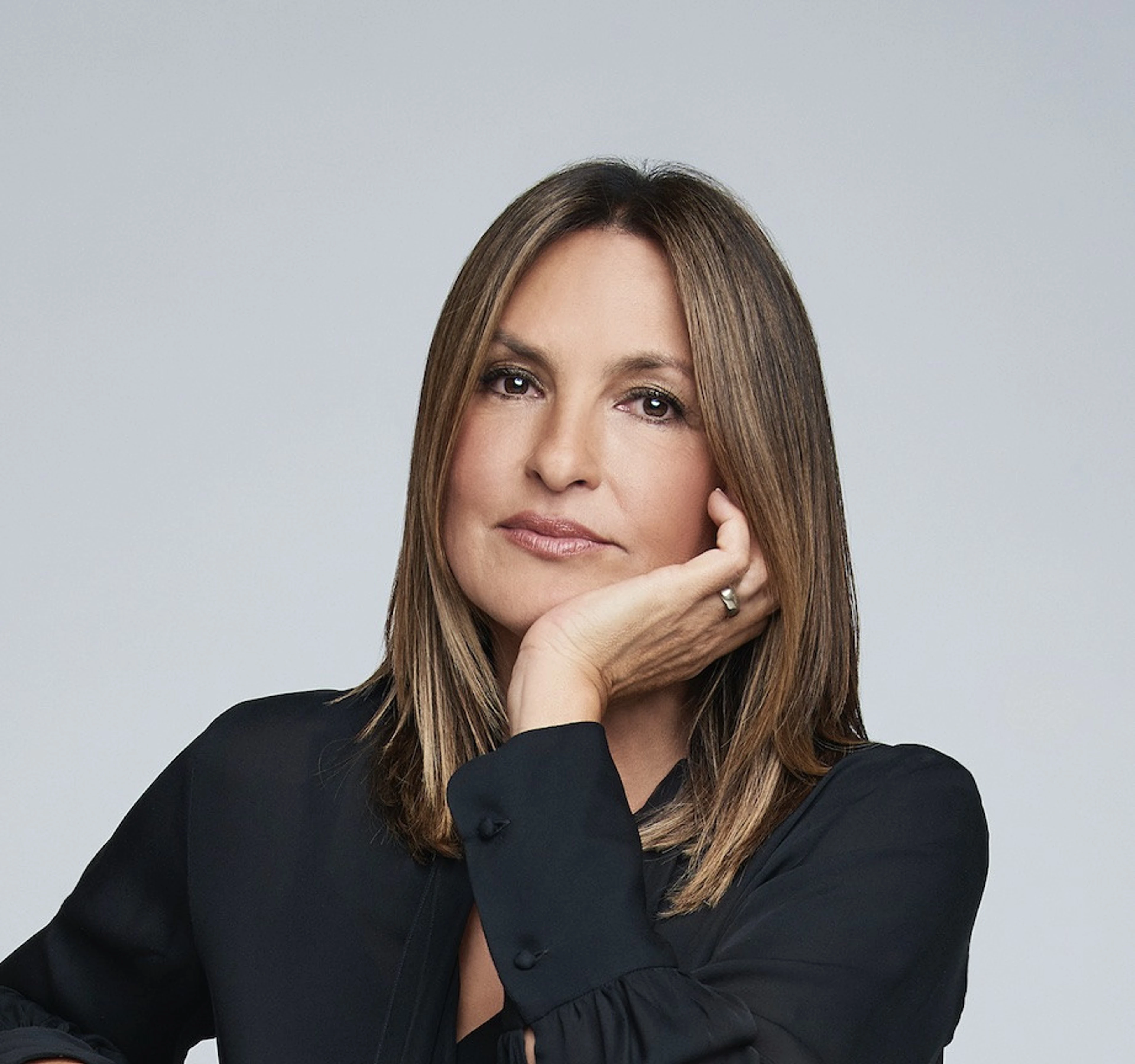 Mariska Hargitay looks toward the camera, resting her face on her hand in a black shirt.
