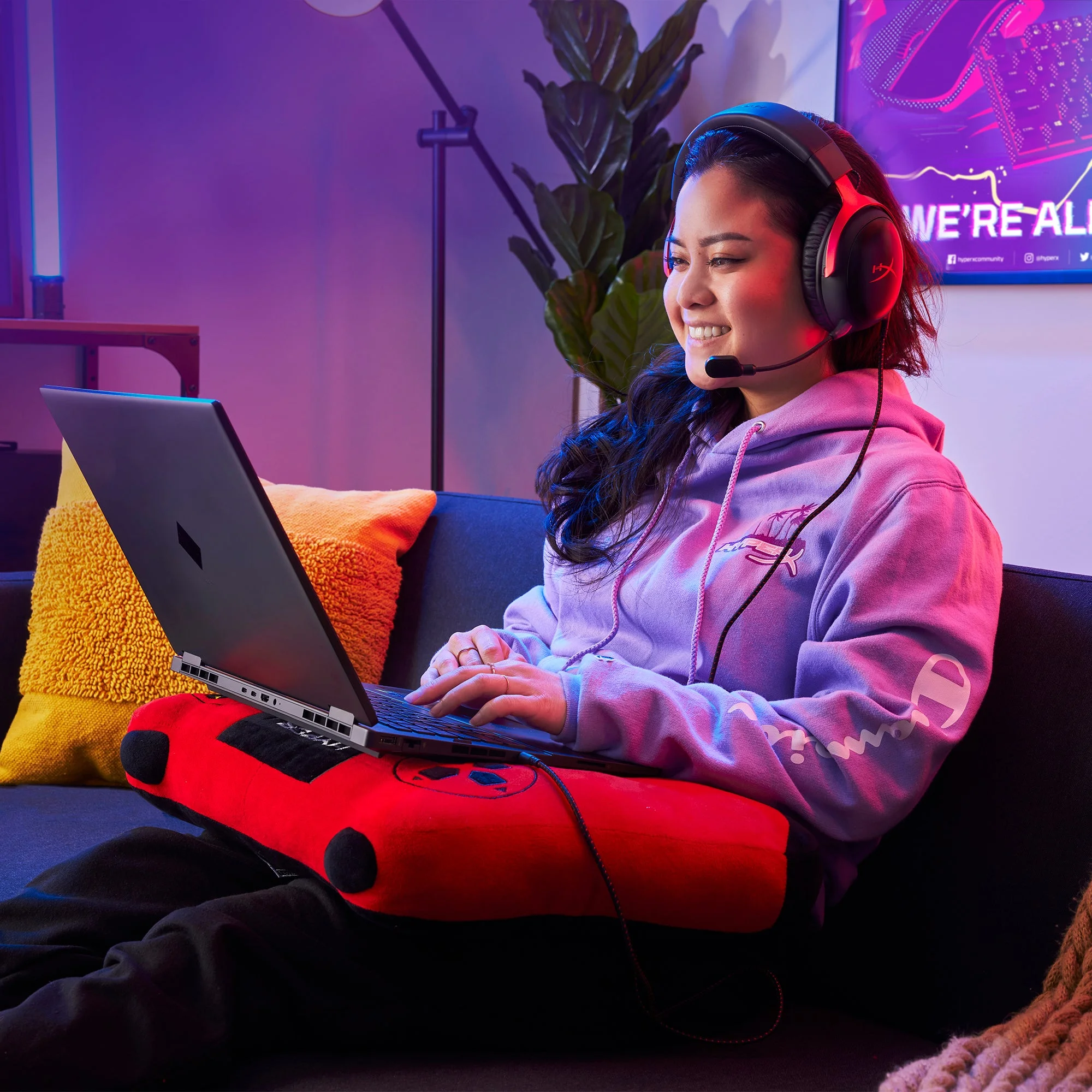 A person wearing the black and red HyperX Cloud III while playing on a laptop on a couch