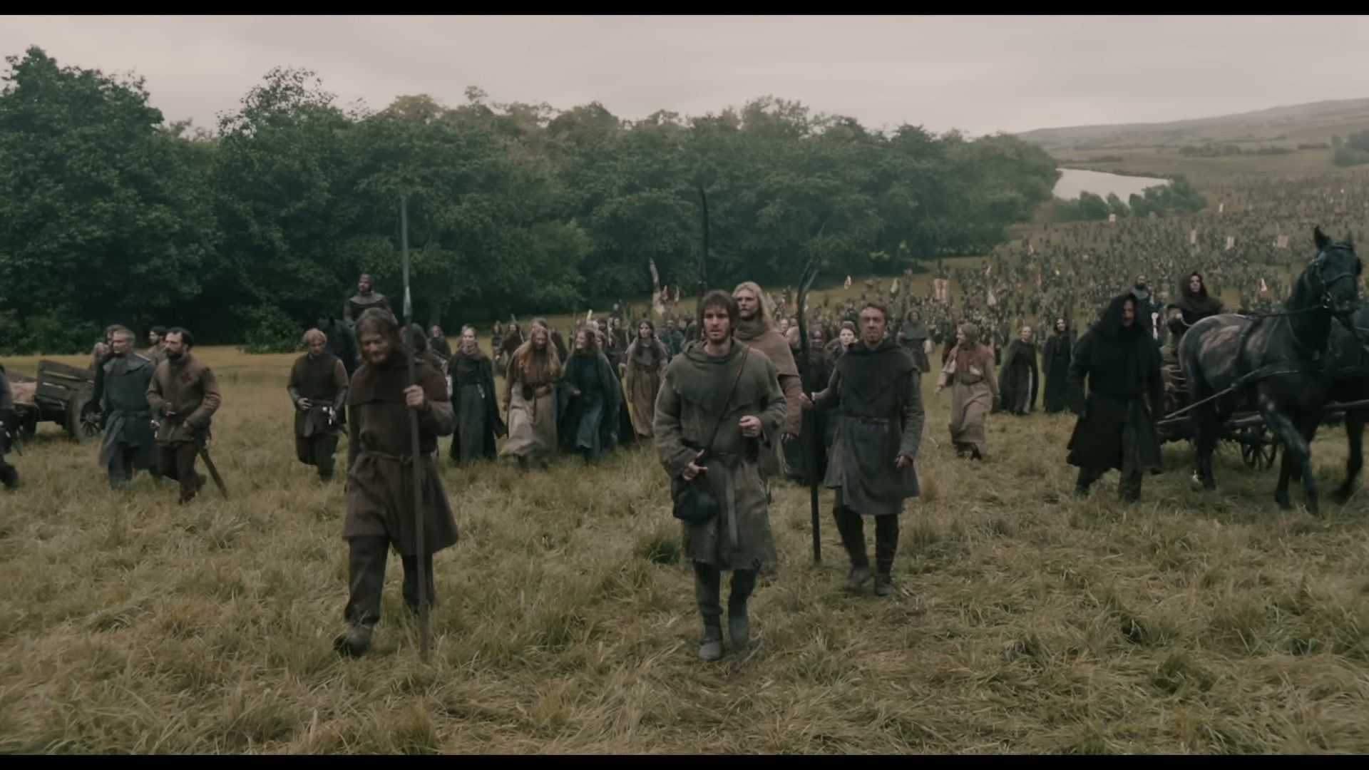 The Ploughman walks at the front of a large group crossing a field.