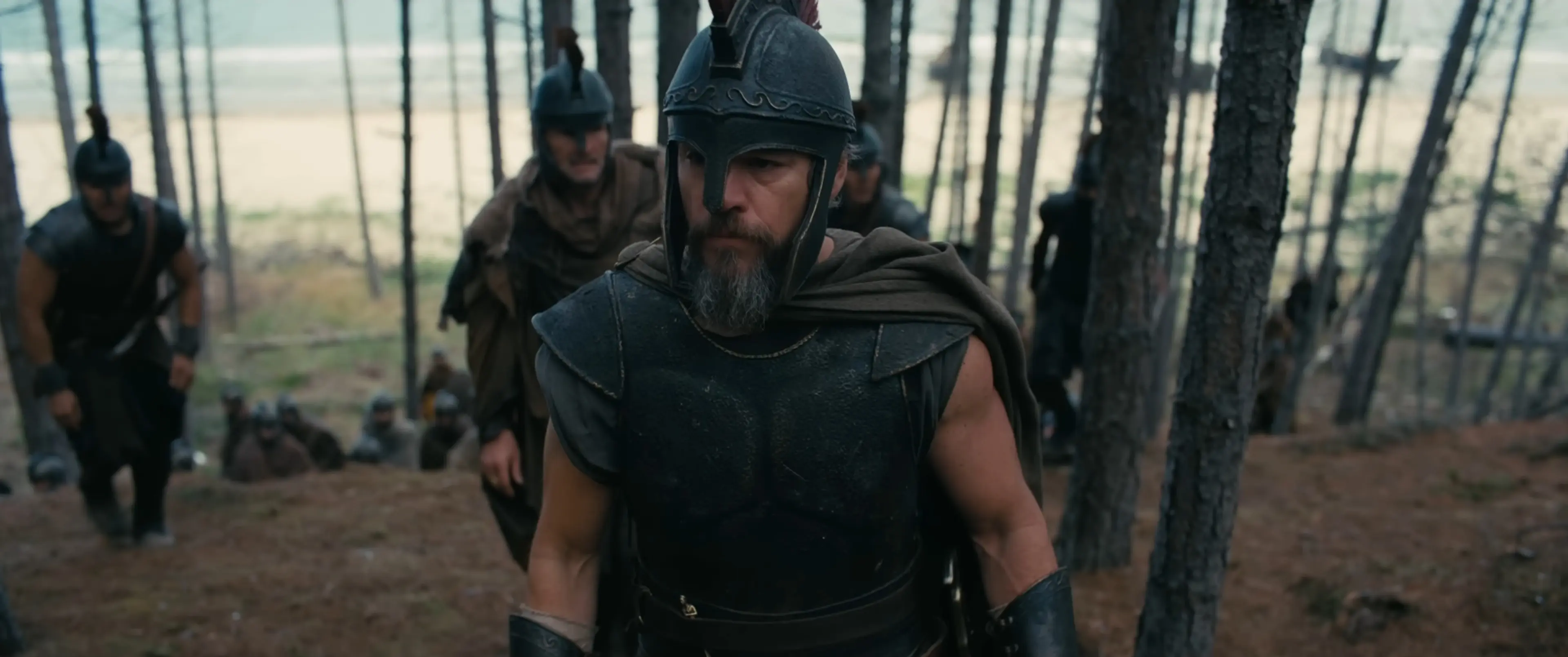 Matt Damon as Odysseus leading armored soldiers through a wooded landscape in The Odyssey.