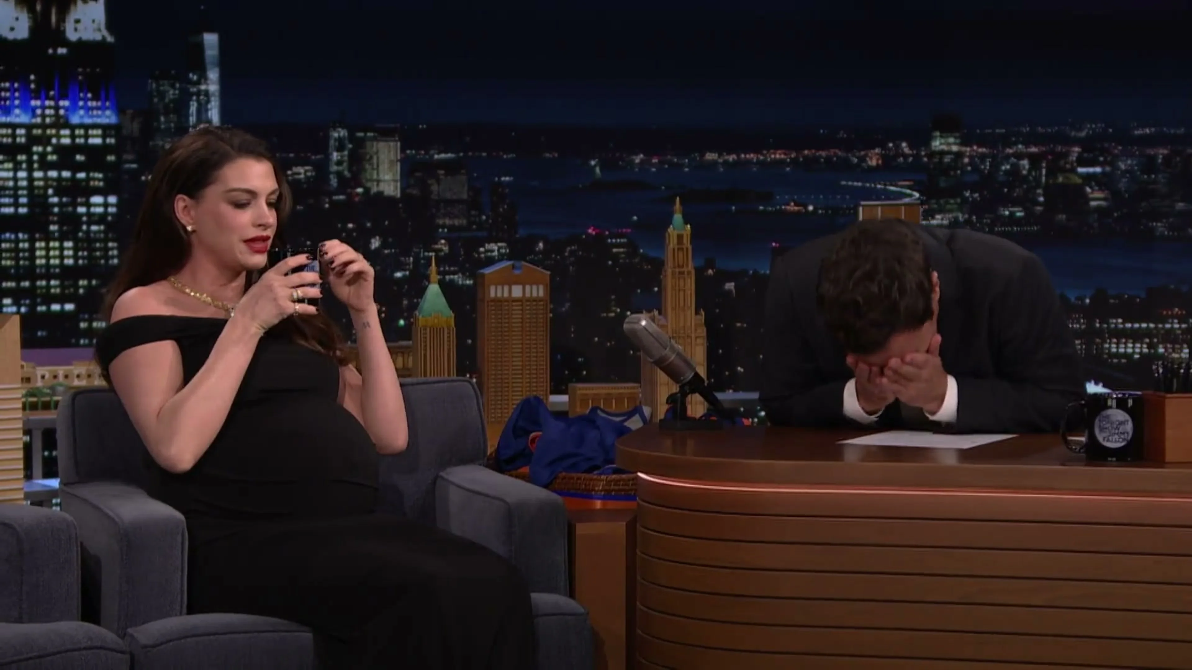 Anne Hathaway holds her coffee cup while Jimmy Fallon laughs during their Verity interview.