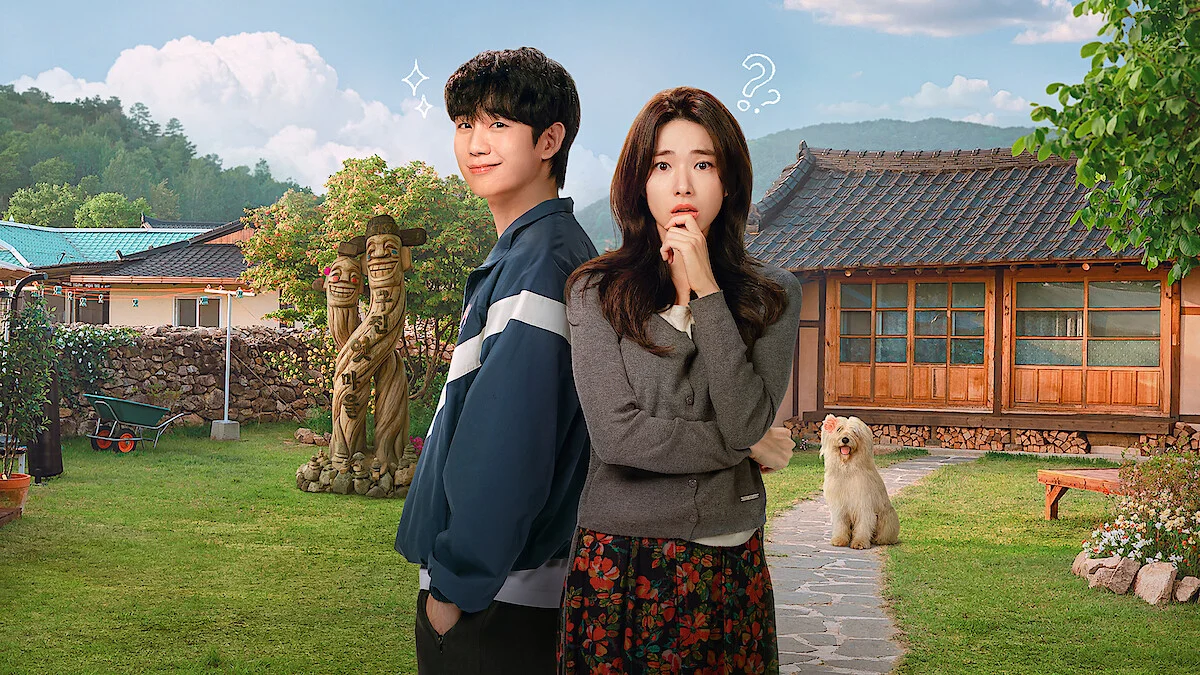 Jung Hae-in and Ha Young stand back to back in a sunny yard beside a traditional house and a small white dog.