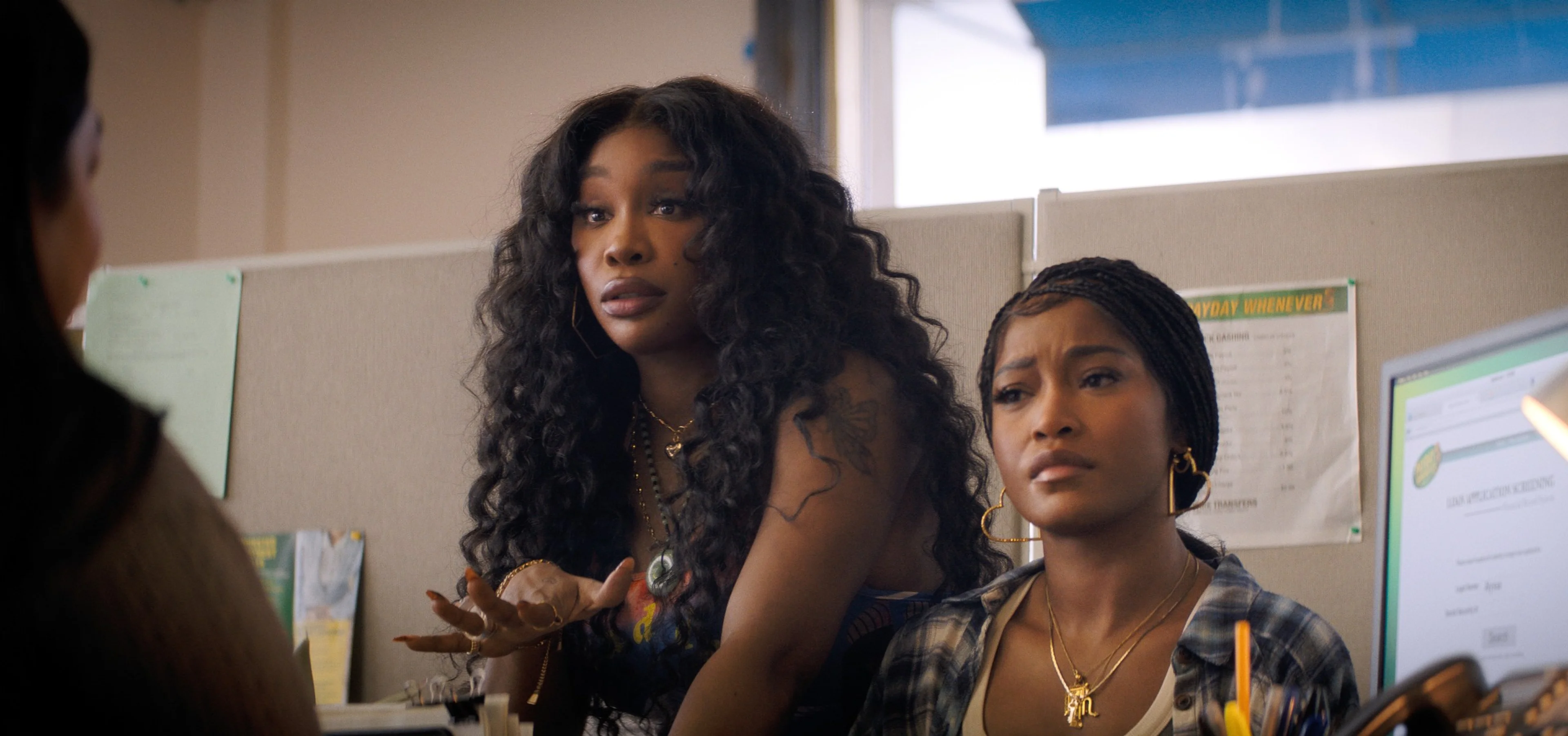 SZA leans forward beside Keke Palmer at a desk in the payday-loan office.