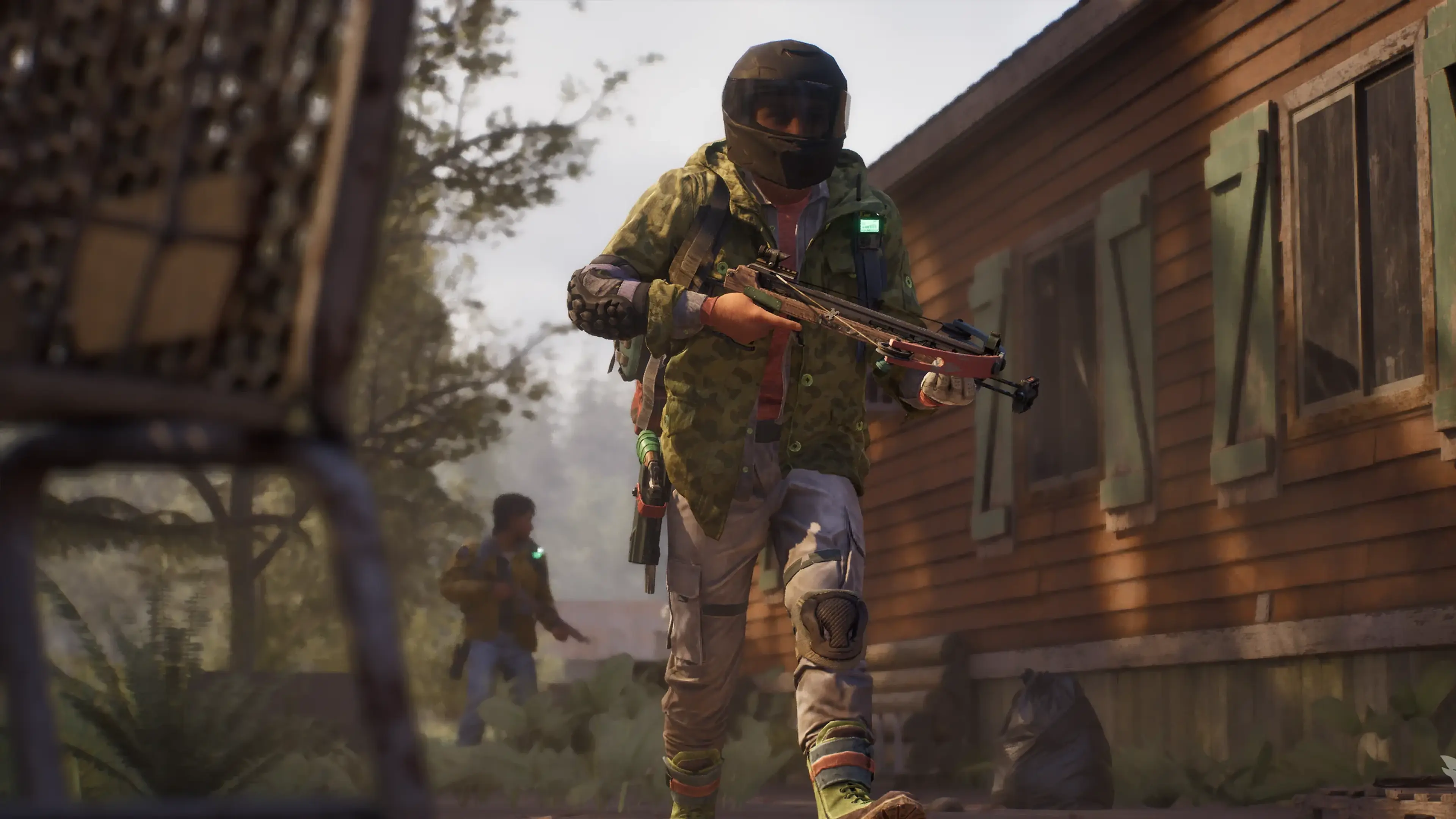 A State of Decay 3 survivor in a helmet carries a crossbow outside a rural building.